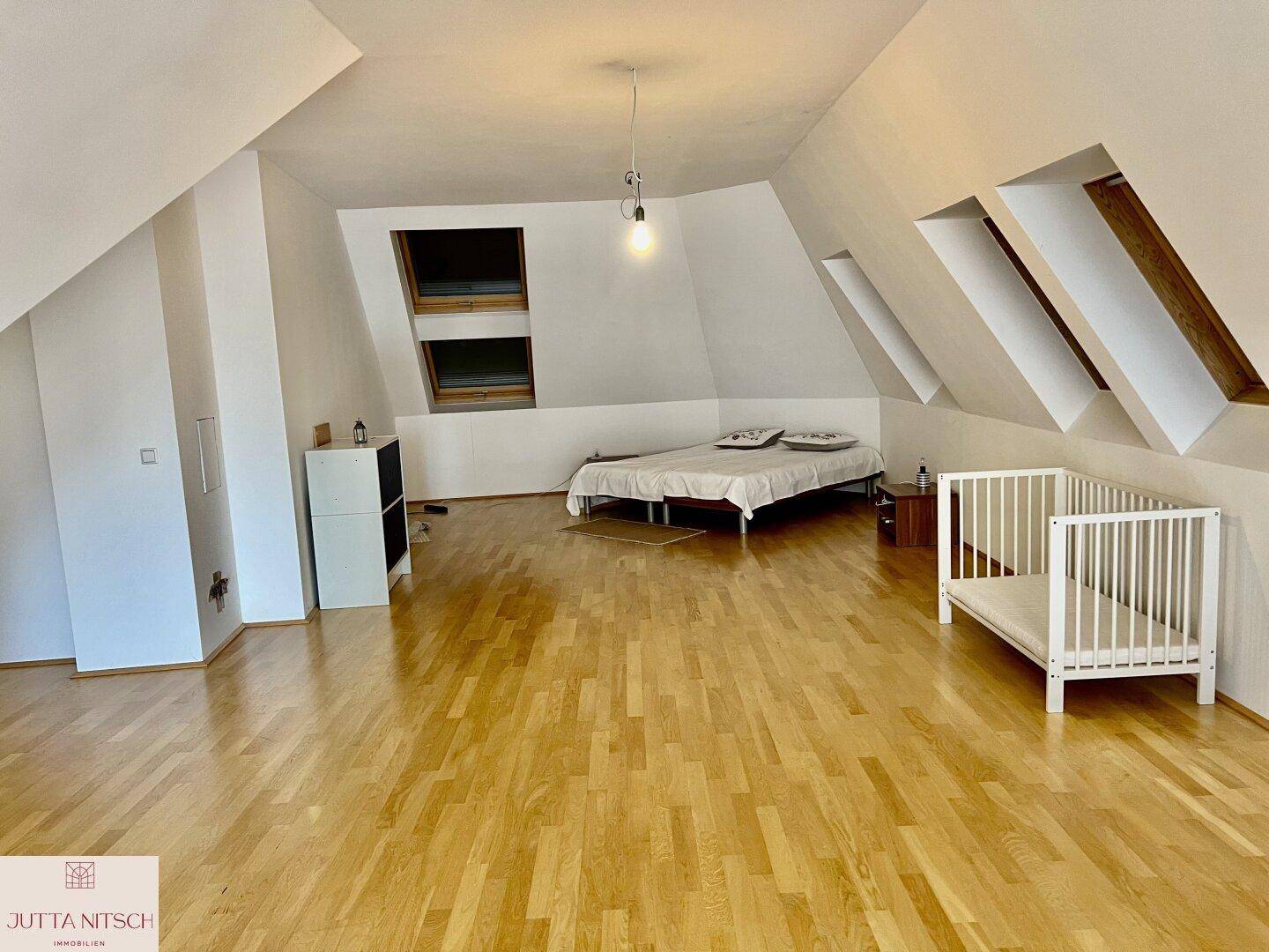Heller Dachbodenraum, eingerichtet als Schlafzimmer, mit Holzparkett und mehreren Dachfenstern.