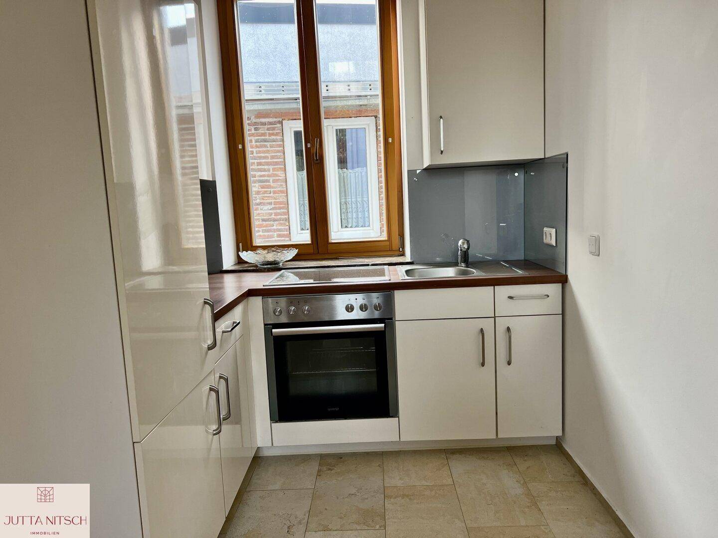 Kleine Küchenzeile mit weißen Schränken, integriertem Backofen und einem Fenster.