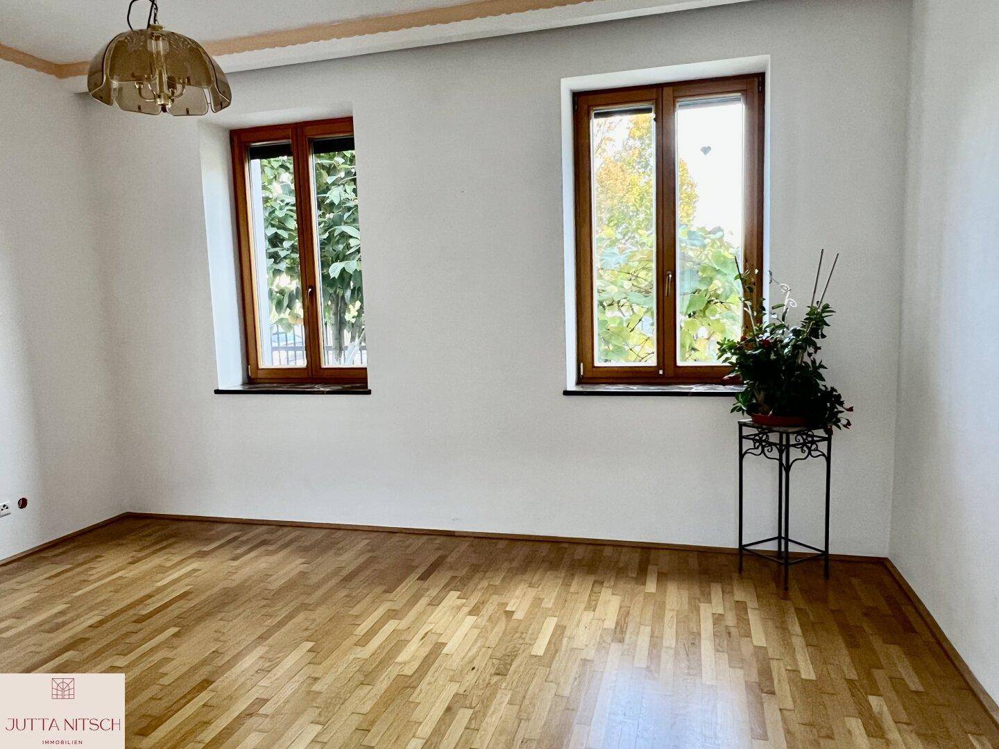 Leerer Raum mit Parkettboden, großen Fenstern und viel natürlichem Lichteinfall.