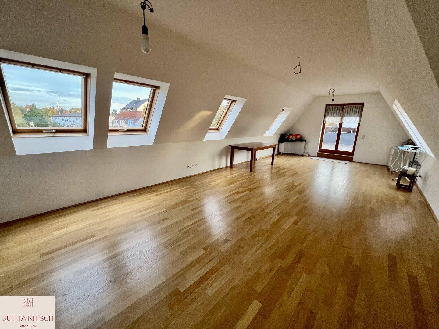 Geräumiger Dachbodenraum mit Holzparkett, großen Dachfenstern und Zugang zu einem kleinen Balkon.