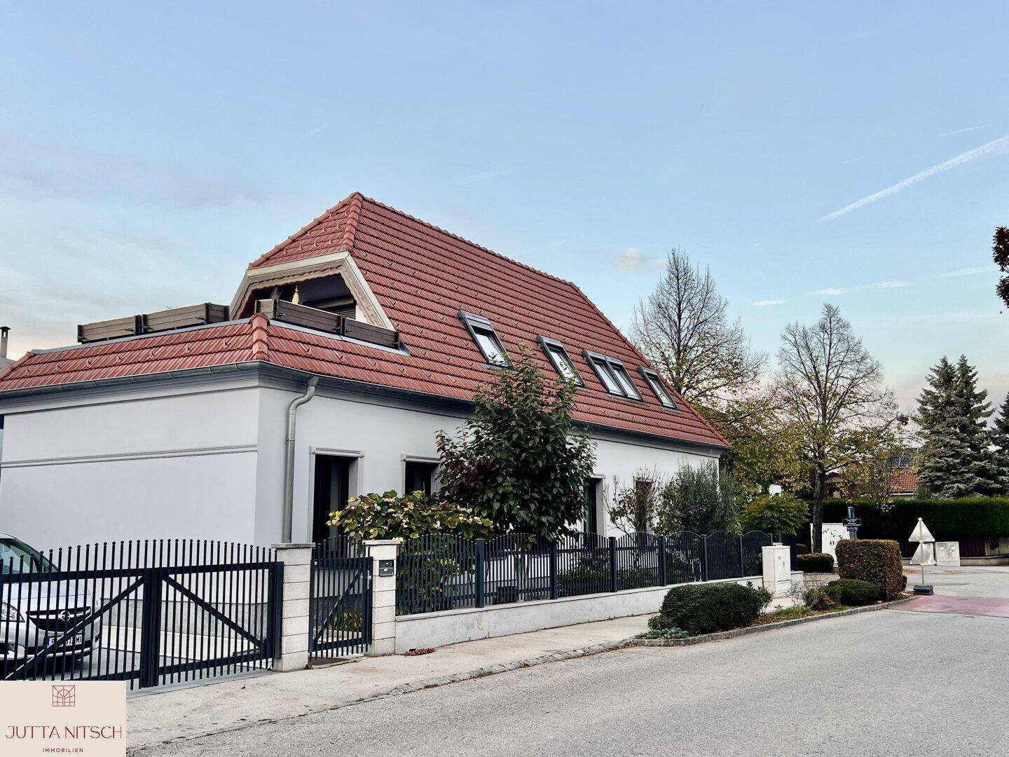 Einfamilienhaus mit rotem Ziegeldach und gepflegtem Vorgarten in der Abenddämmerung.