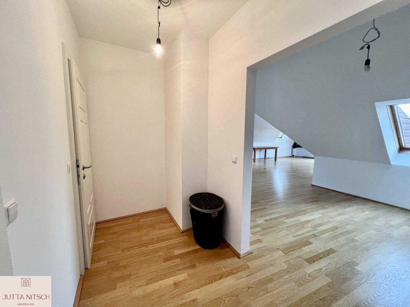 Heller Flurbereich im Dachgeschoss mit Holzparkett und Zugang zu weiteren Räumen.