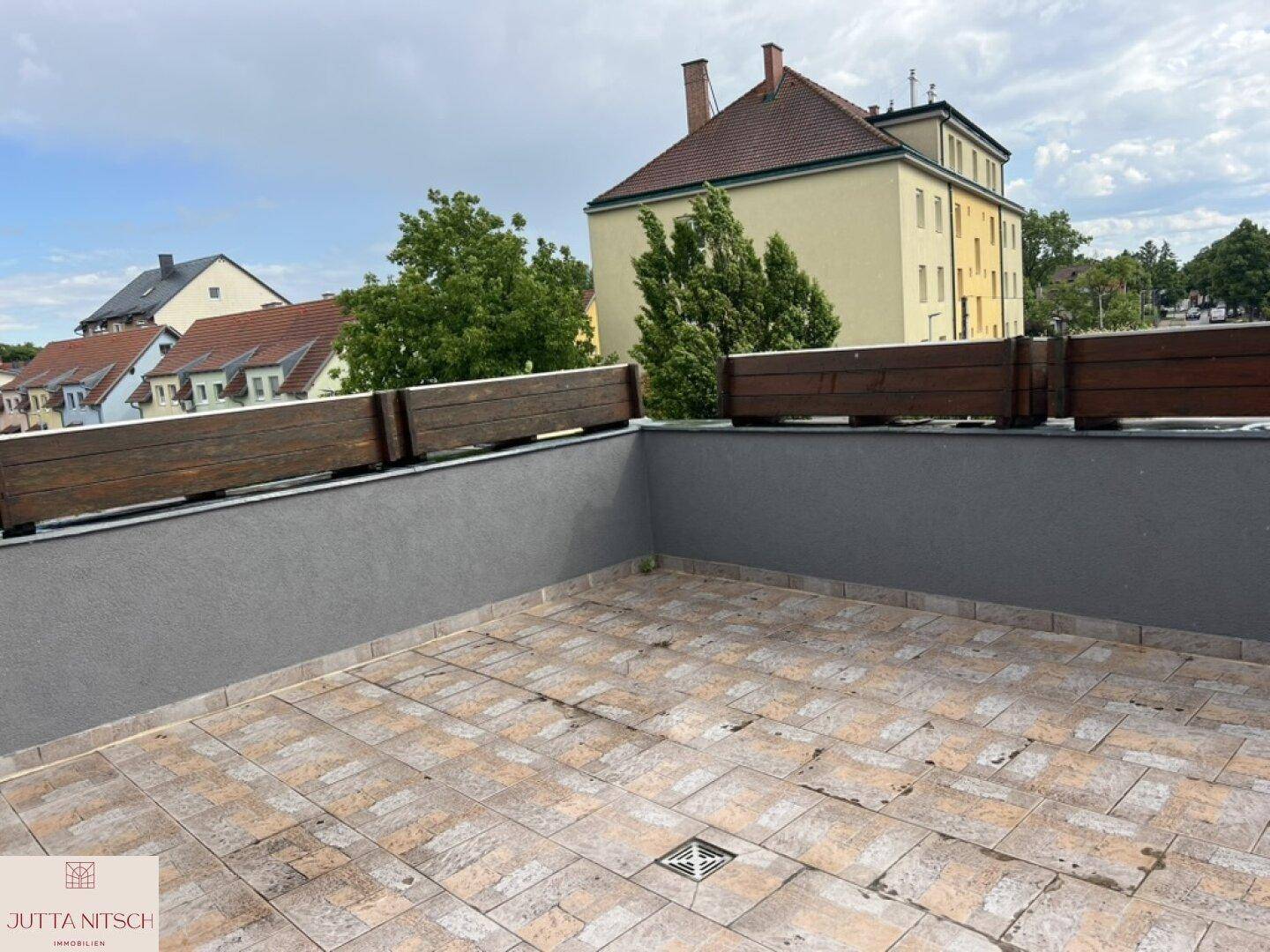 Große, geflieste Dachterrasse mit Holzelementen und Blick auf die umliegenden Gebäude.