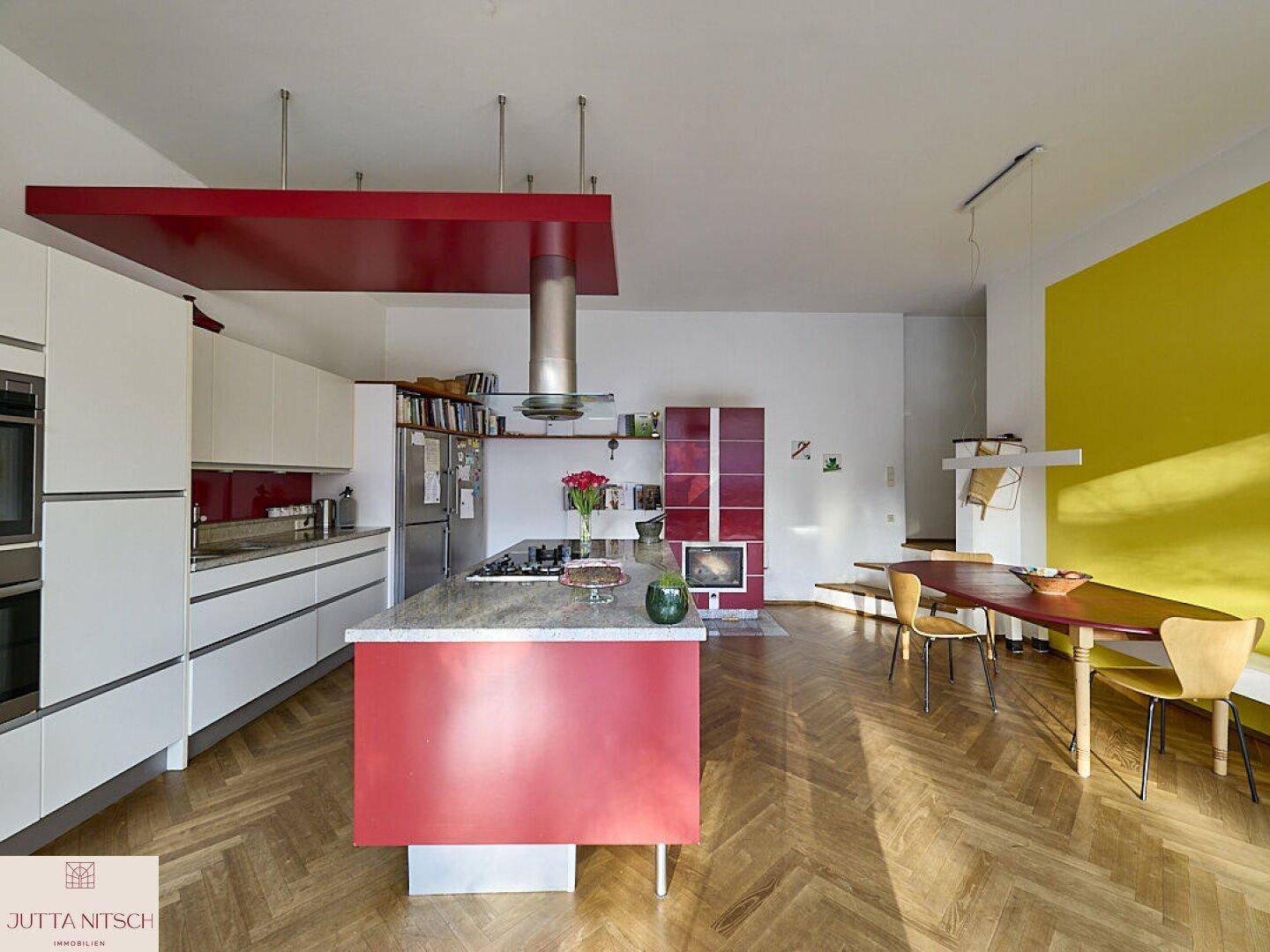 Moderne offene Küche mit roter Kücheninsel, Parkettboden und angrenzendem Essbereich mit gelber Wand.
