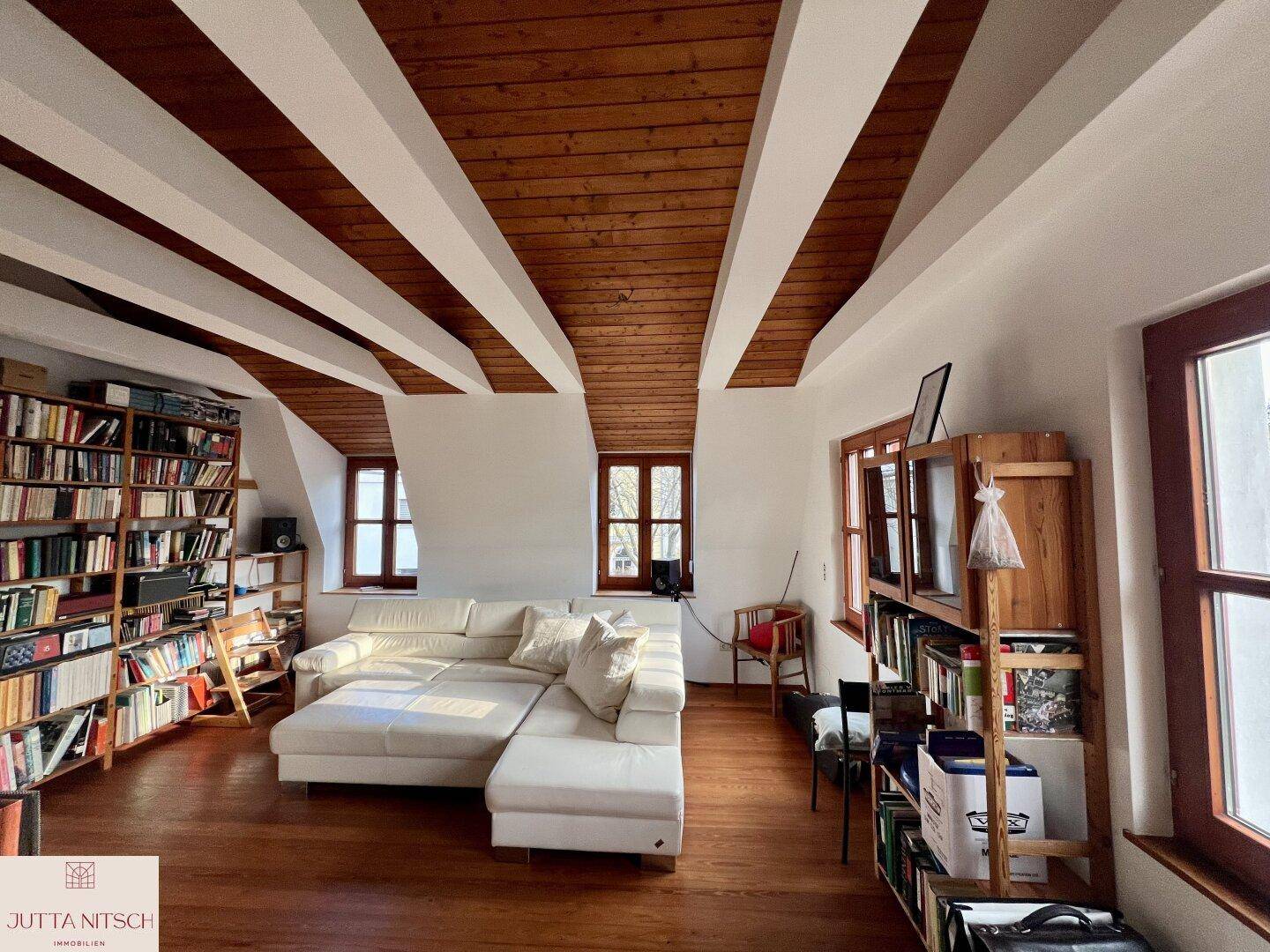 Geräumiges Wohnzimmer im Dachgeschoss mit Holzbalken, vielen Büchern und gemütlicher Sofalandschaft.