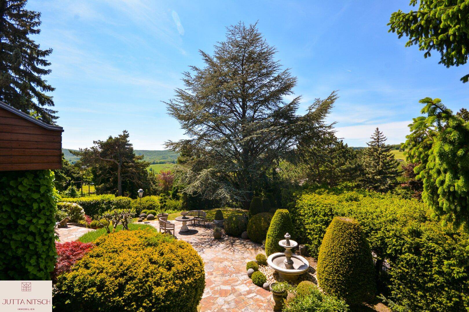 Weitläufiger Garten mit Panoramablick, Steinterrasse und üppiger, gepflegter Vegetation.