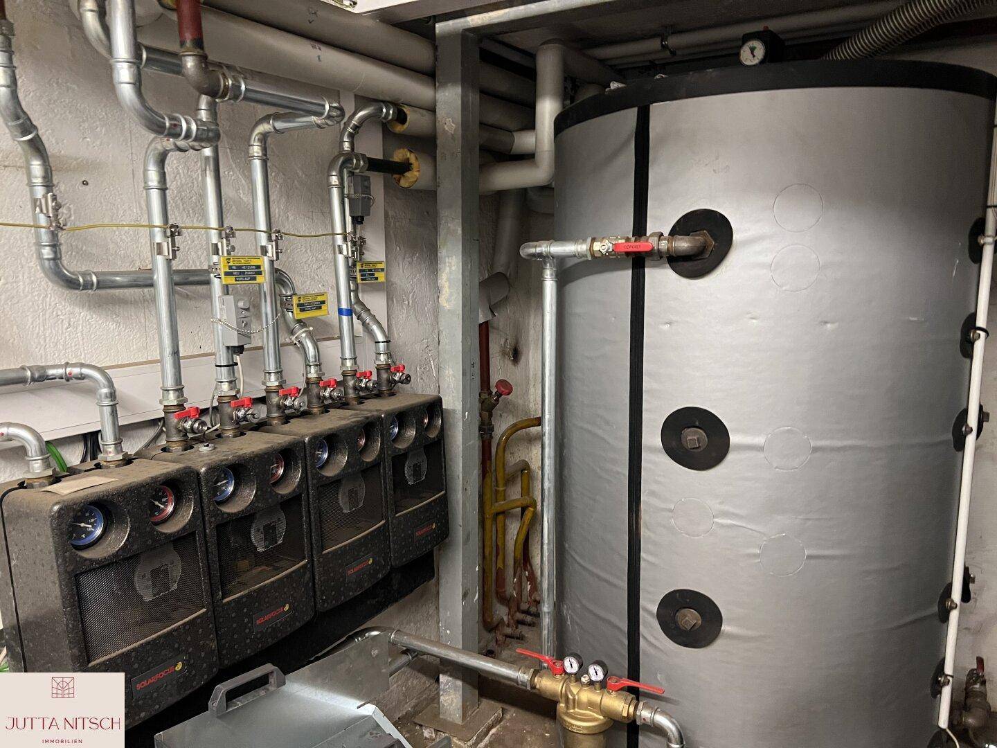 Technikraum mit Heizungsanlage, Warmwasserspeicher und zahlreichen Rohrleitungen.