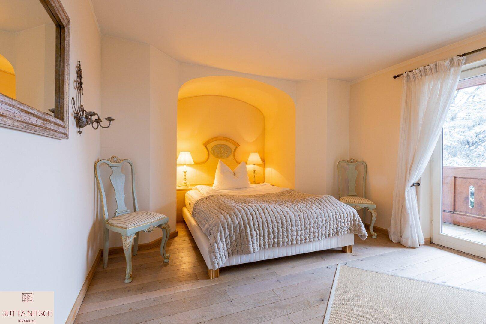 Gemütliches Schlafzimmer mit Holzboden, Nische für das Bett und Zugang zum Balkon.