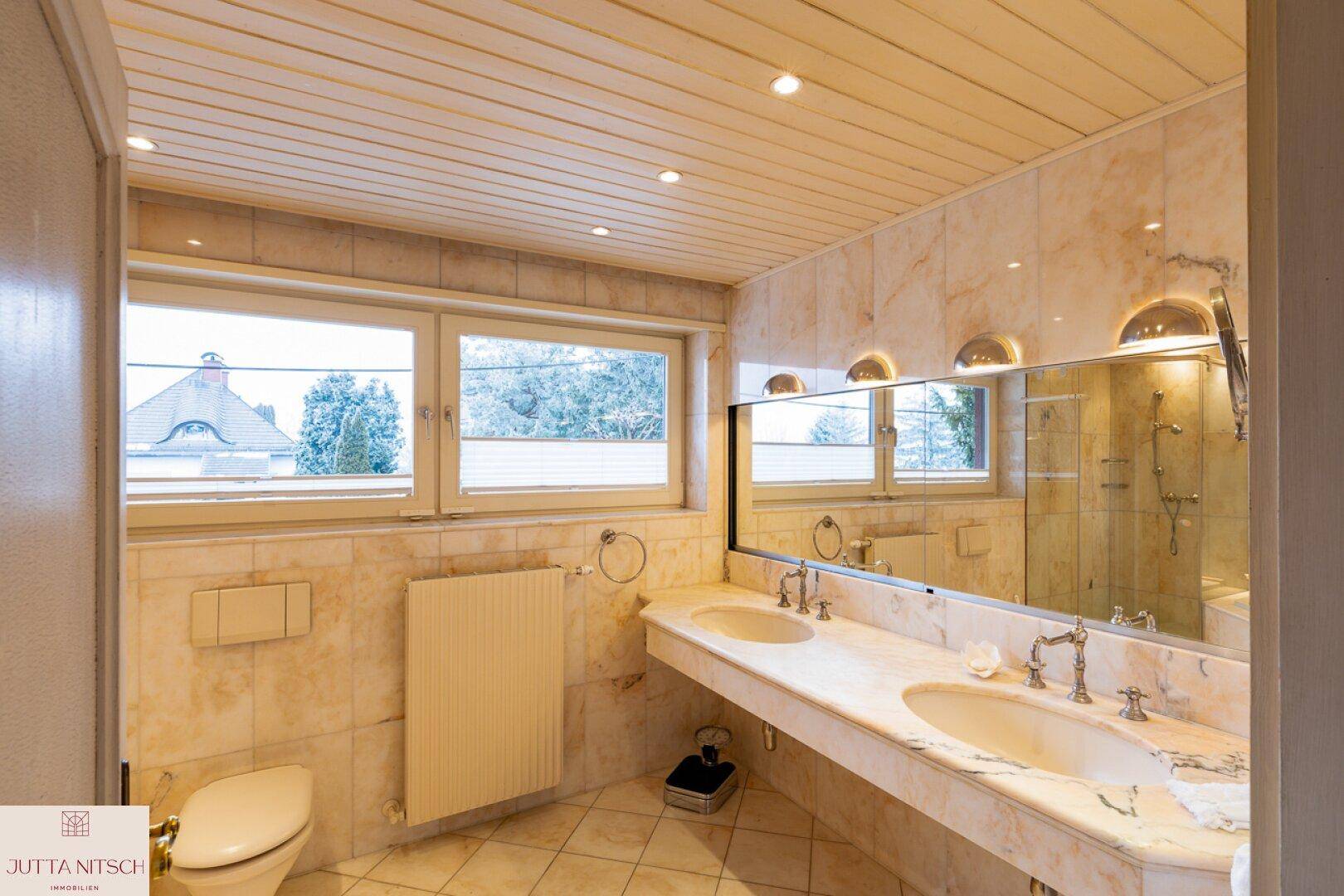 Helles Badezimmer mit Doppelwaschbecken, Marmorfliesen und Fenster.