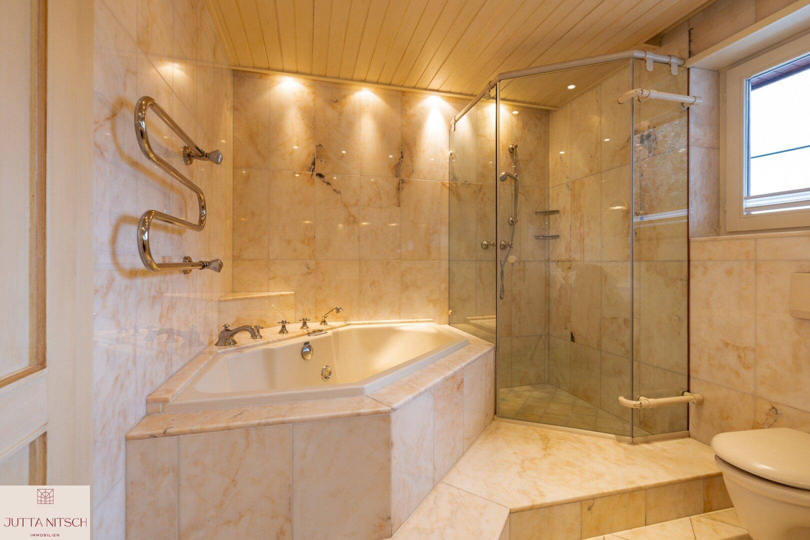 Geräumiges Badezimmer mit Eckbadewanne, Duschkabine, Marmorfliesen und Fenster.