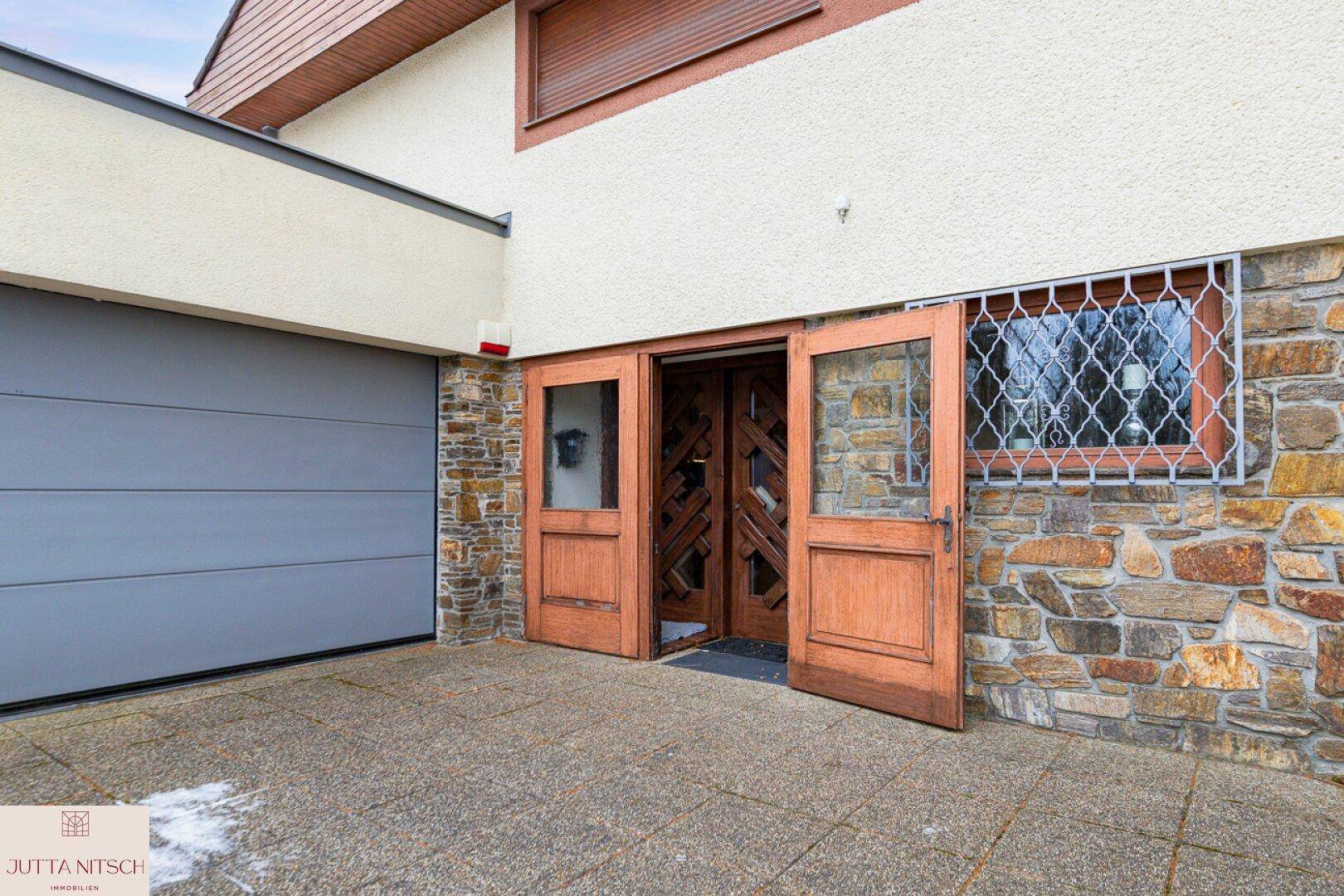 Hauseingang mit Holztüren, Steinfassade und angrenzender Garage.