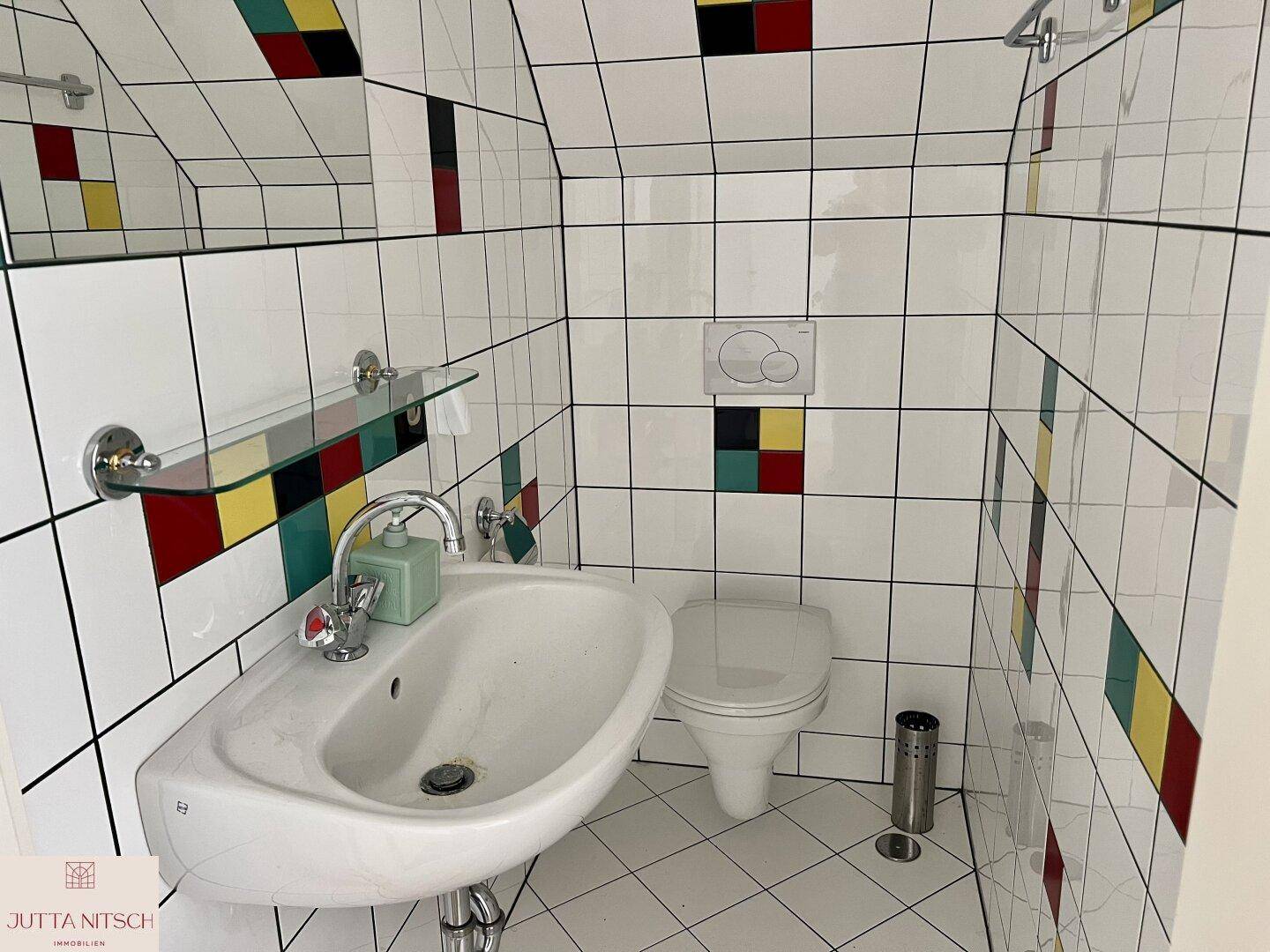 Buntes Badezimmer mit weißen Fliesen und farbigen Akzenten, ausgestattet mit Waschbecken und Toilette.