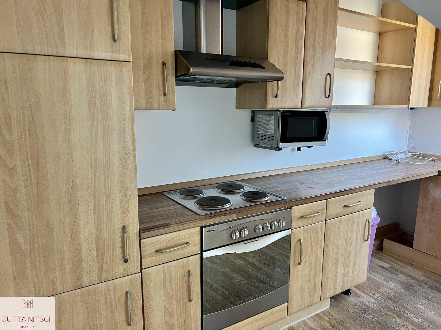Funktionale Holzküche mit Einbaugeräten, Herd, Backofen und Mikrowelle, bereit zur Nutzung.