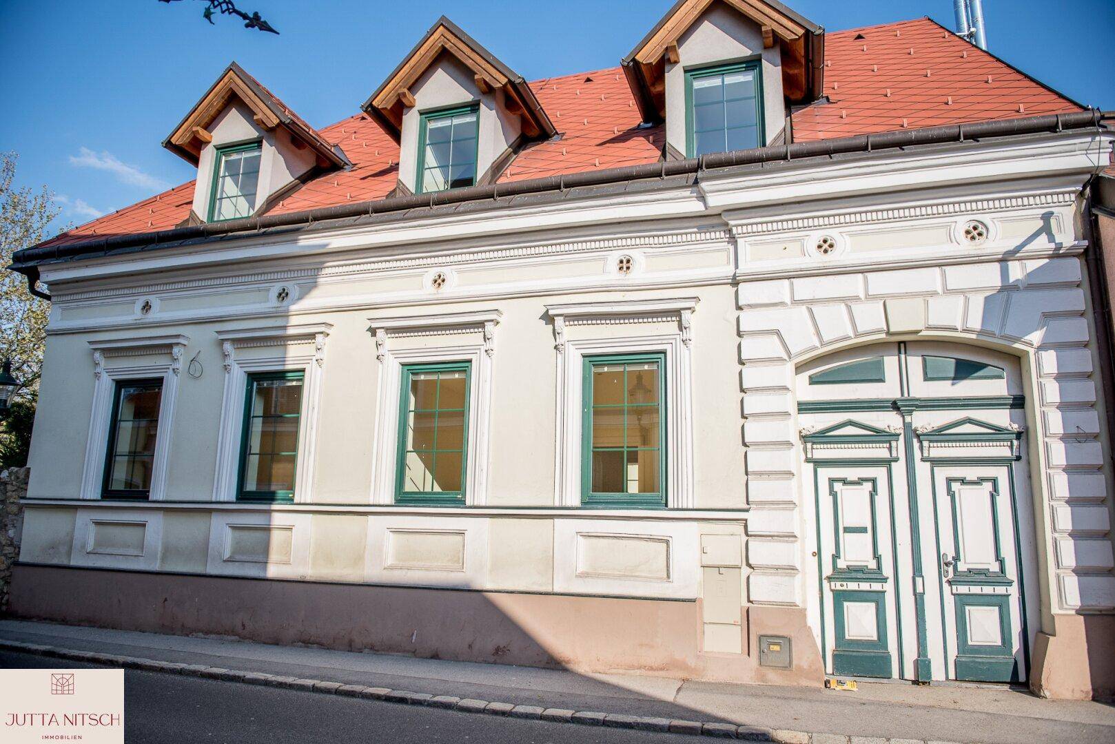Historische Fassade eines Gebäudes mit verzierten Fenstern, grünen Fensterläden und einem großen Tor.