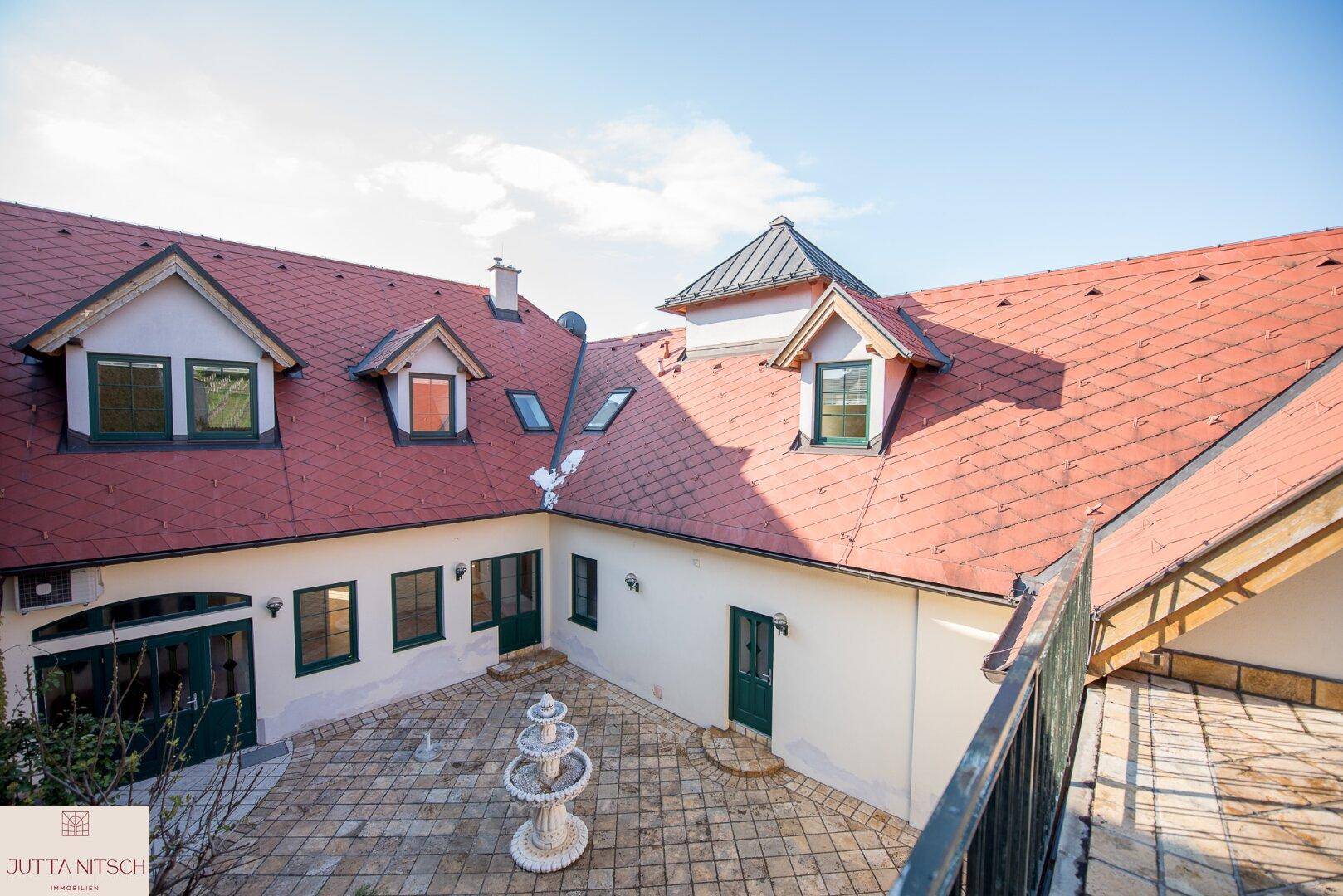 Innenhof mit gepflastertem Bereich, einem Brunnen und Blick auf die roten Ziegeldächer des Gebäudes.