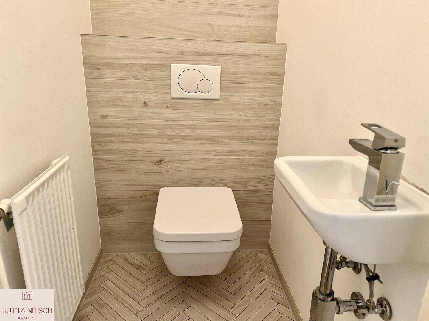 Modernes Gäste-WC mit wandhängender Toilette und kleinem Waschbecken, stilvoll gefliest.