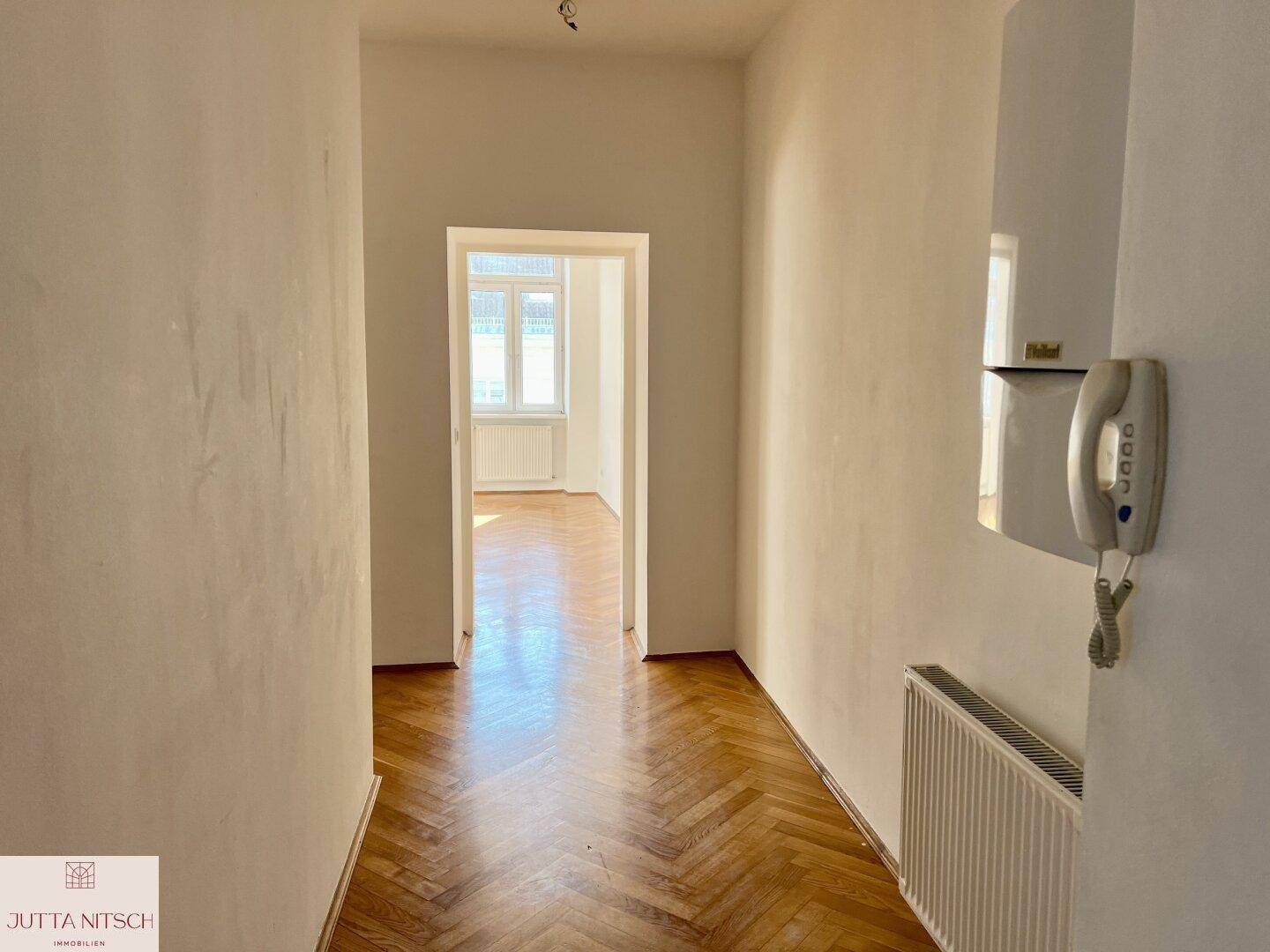 Langer Flur mit Fischgrätparkett und Gegensprechanlage, der zu hellen Wohnbereichen führt.