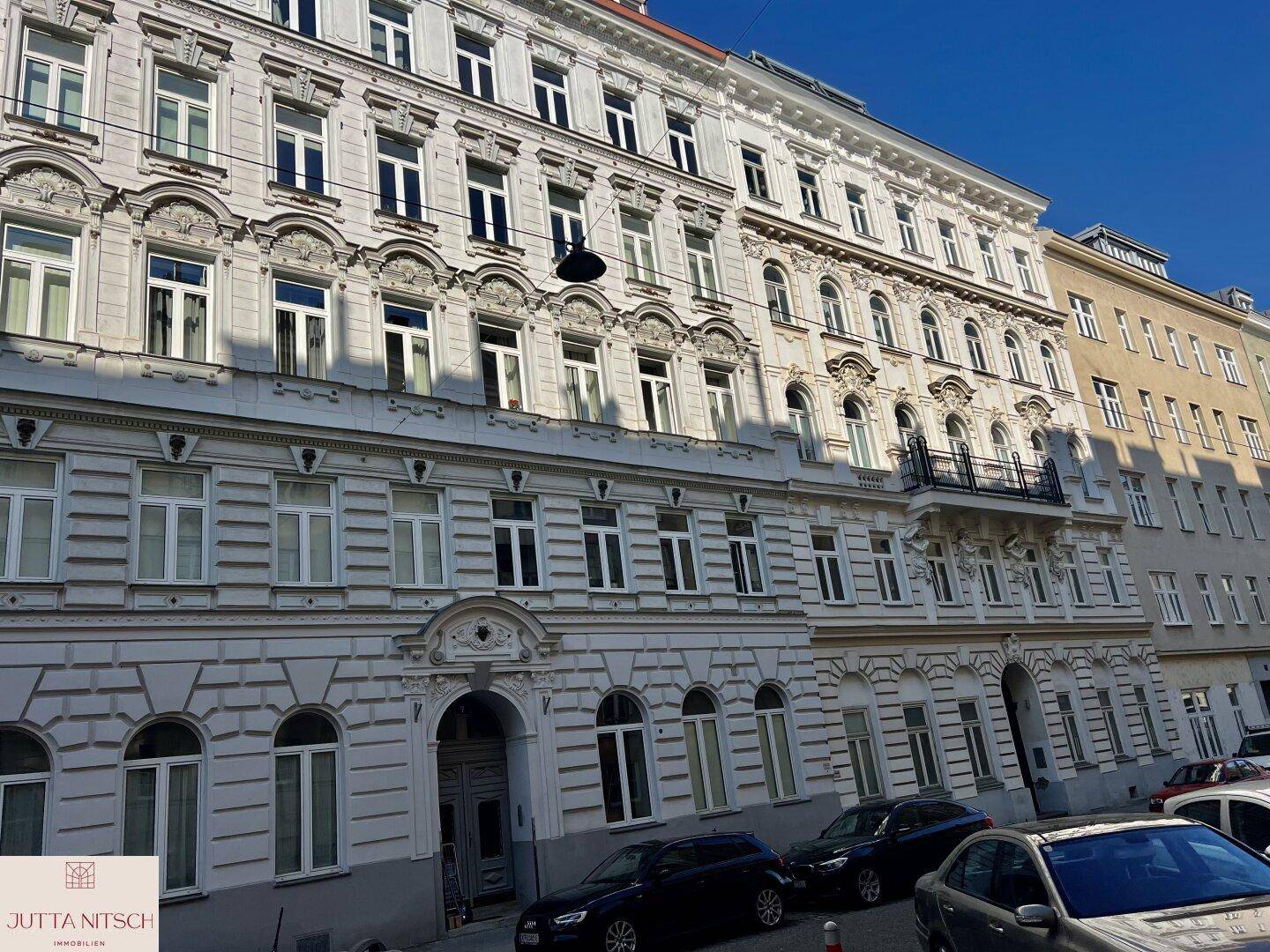 Eindrucksvolle Altbaufassade mit reich verzierten Details und vielen Fenstern an einem sonnigen Tag.