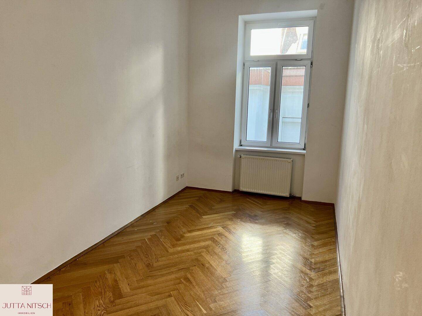Kleinerer Raum mit Fischgrätparkett und einem Fenster, ideal als Schlafzimmer oder Arbeitszimmer.