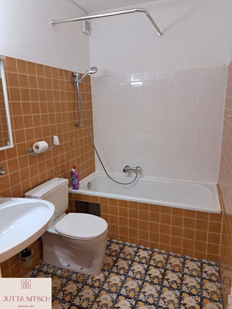 Badezimmer mit Badewanne, Waschbecken und WC, ausgestattet mit braunen Fliesen.
