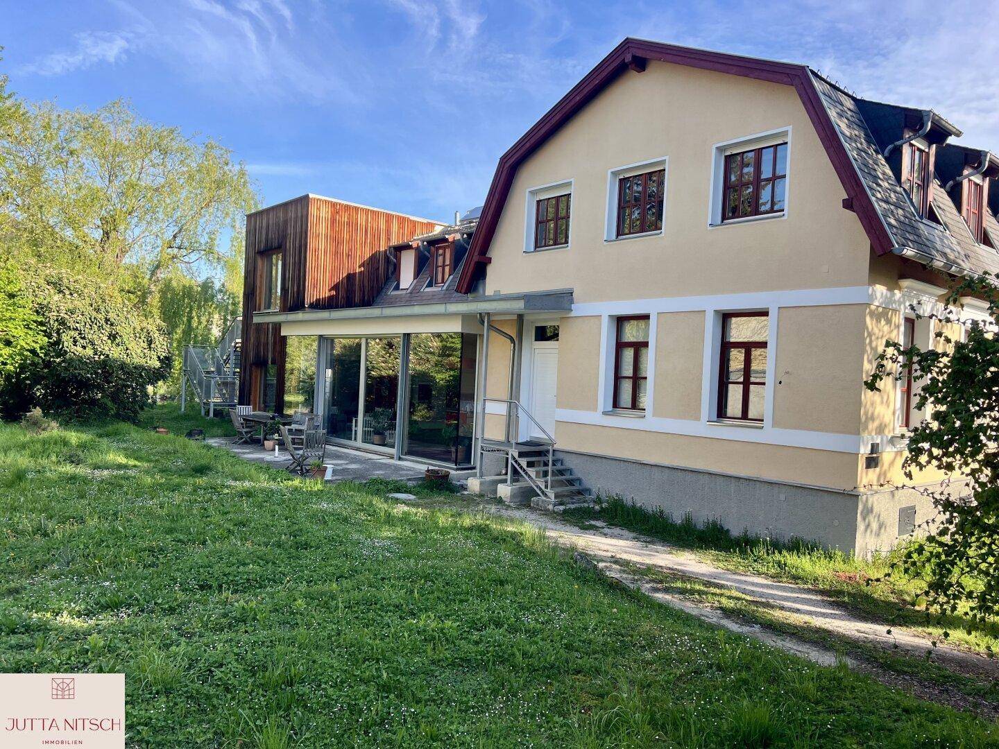 Großzügiges Haus mit moderner Glaserweiterung und weitläufigem Garten unter blauem Himmel.