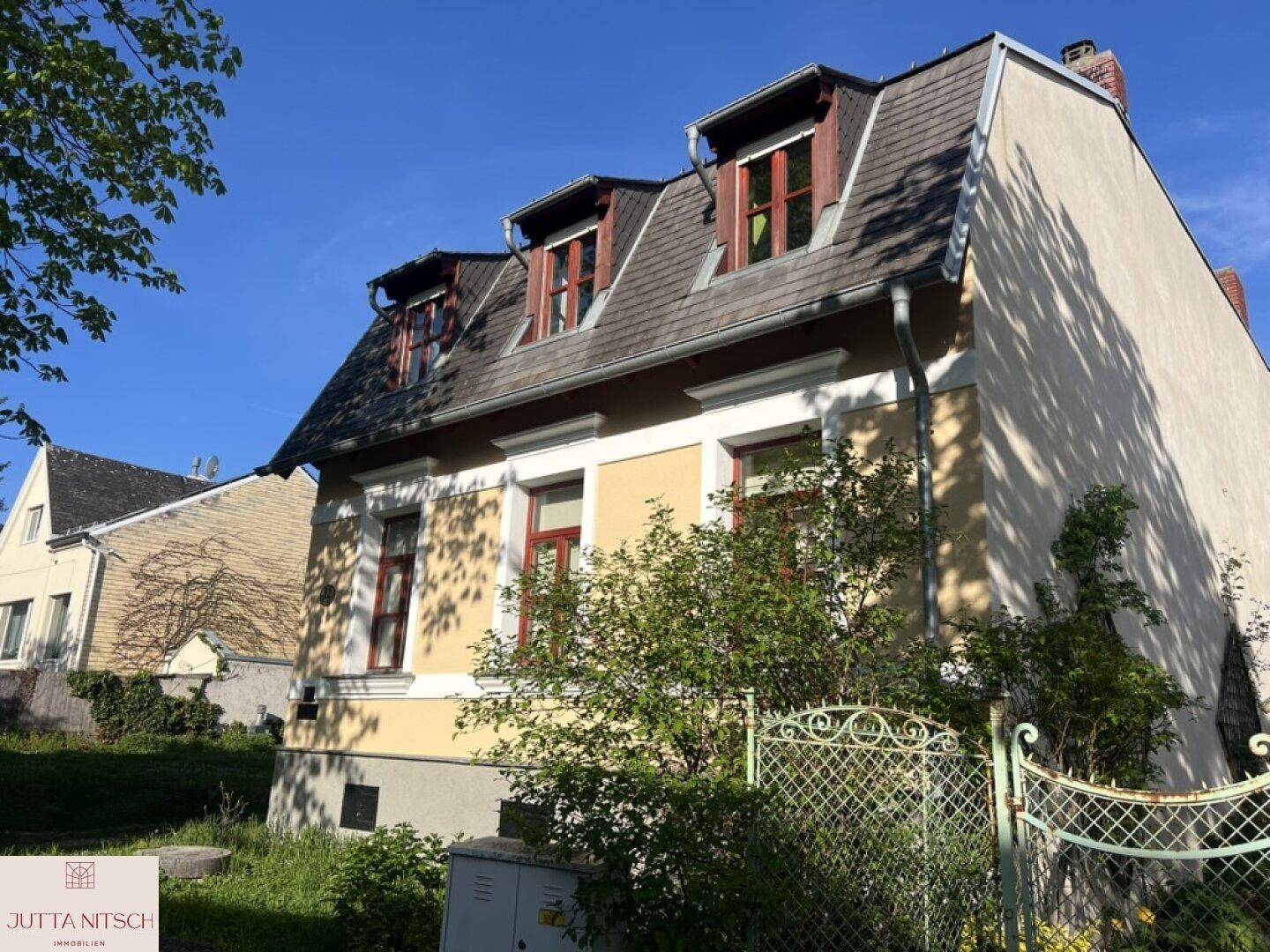 Historisches Gebäude mit gelber Fassade, Mansarddach und Gaubenfenstern unter strahlendem Himmel.
