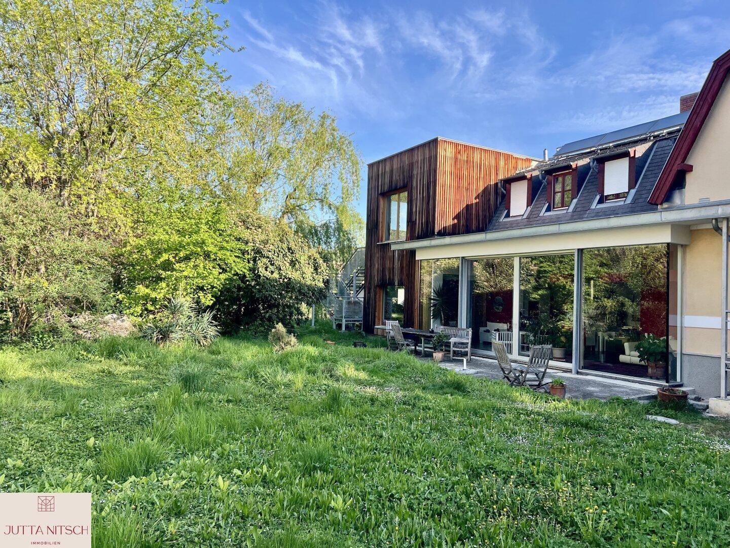 Großer Garten mit Rasenfläche, moderner Holzfassade und bodentiefen Fenstern zur Terrasse.