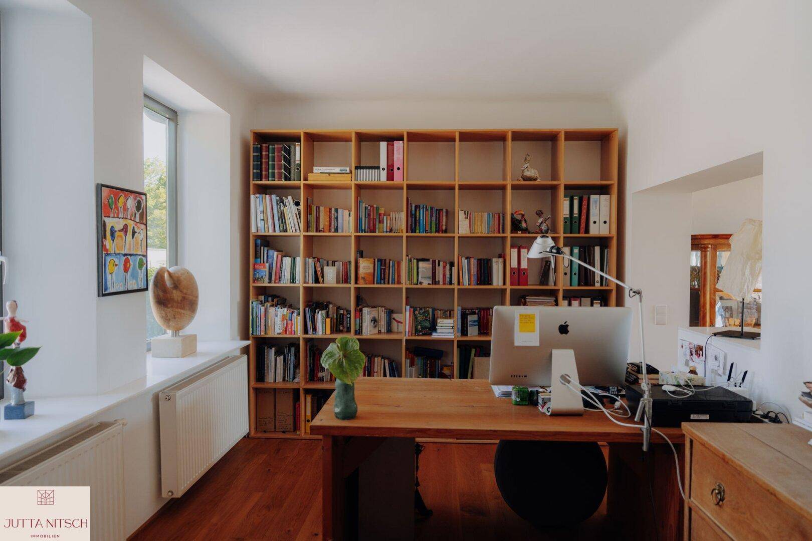 Helles Arbeitszimmer mit großem Bücherregal, Holzschreibtisch und Holzboden.