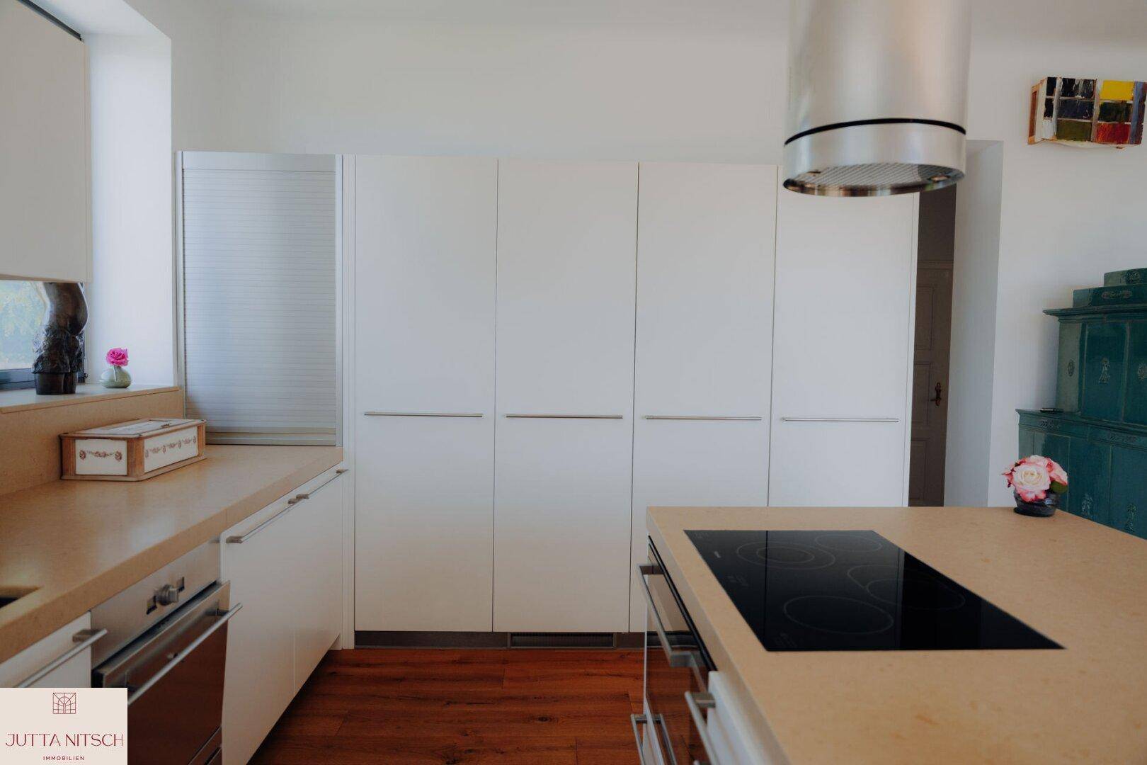 Moderne Küche mit weißen Schränken, Holz-Arbeitsplatte und Induktionskochfeld auf der Kücheninsel.