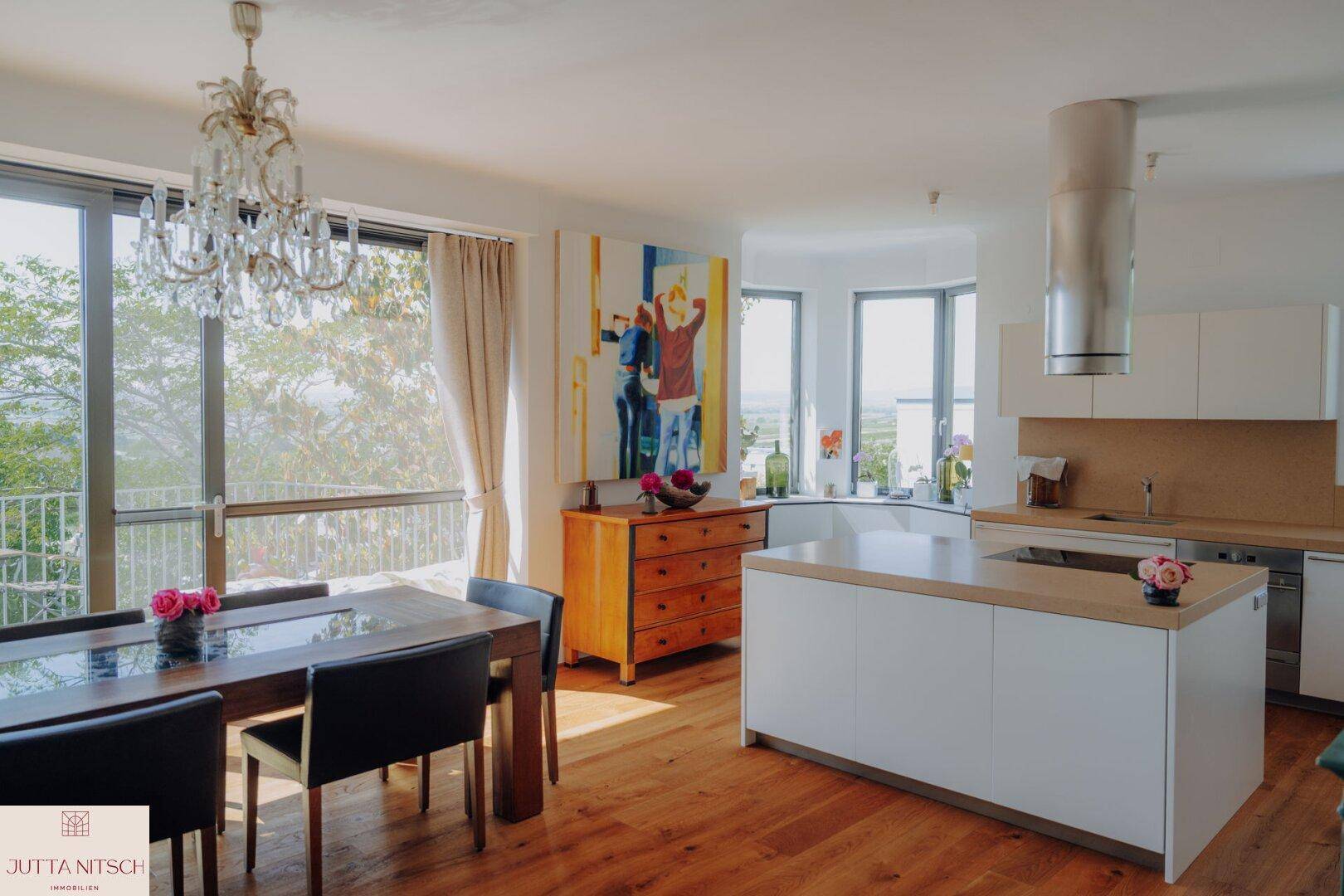 Lichtdurchfluteter Wohn-Essbereich mit moderner Küche, Holzboden und weitem Ausblick durch große Fenster.