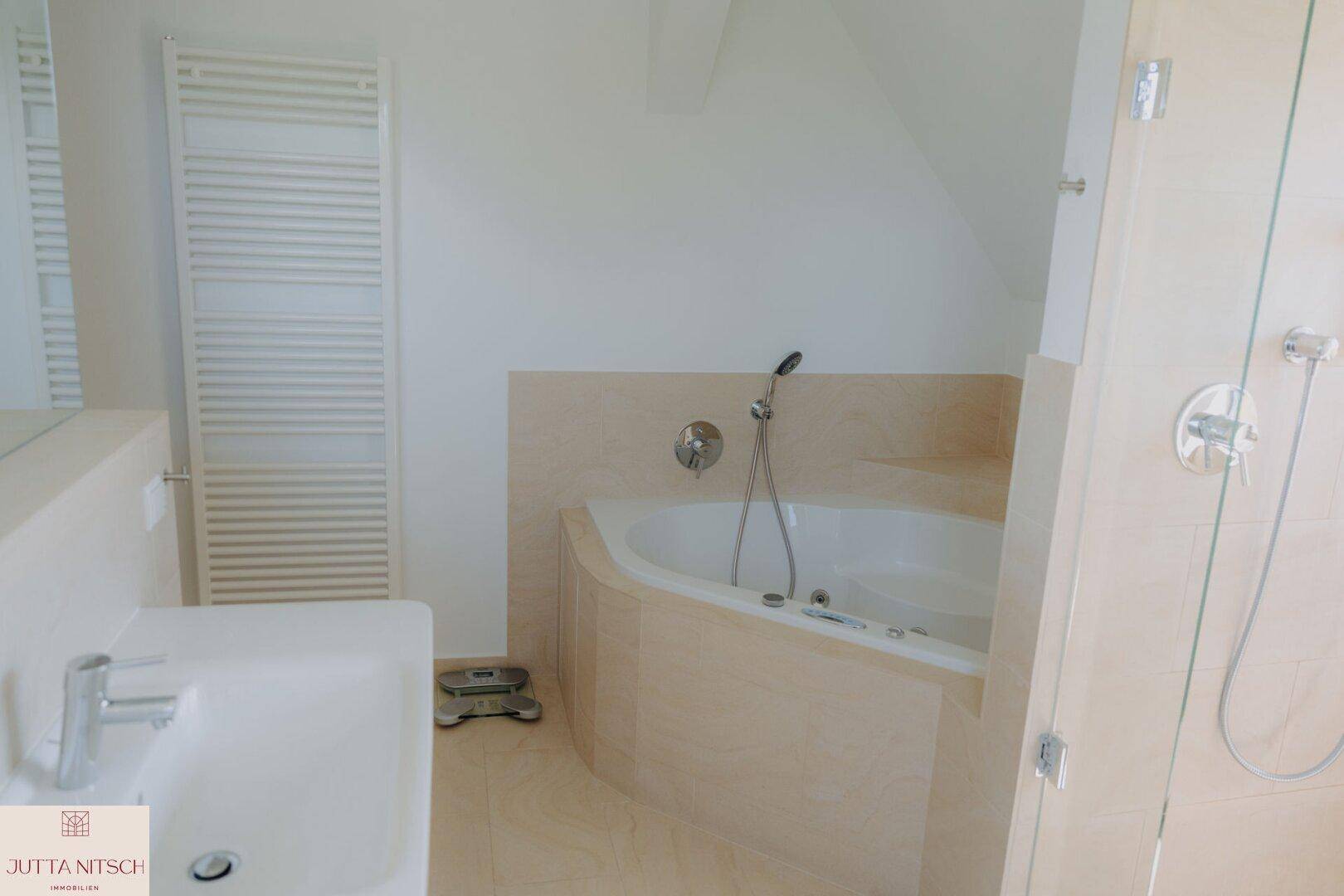Badezimmer mit Eckbadewanne, Einzelwaschbecken und beheiztem Handtuchhalter.