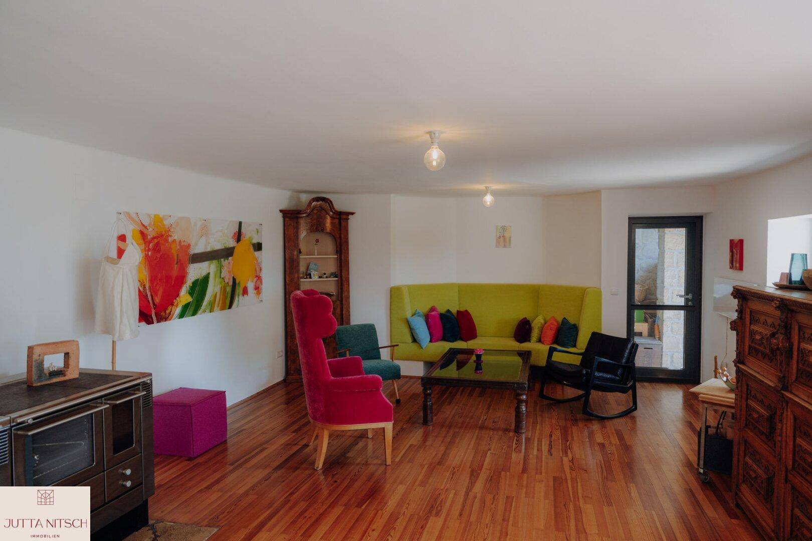 Farbenfrohes Wohnzimmer mit Holzboden, gemütlichen Sitzgelegenheiten und einem Ofen.