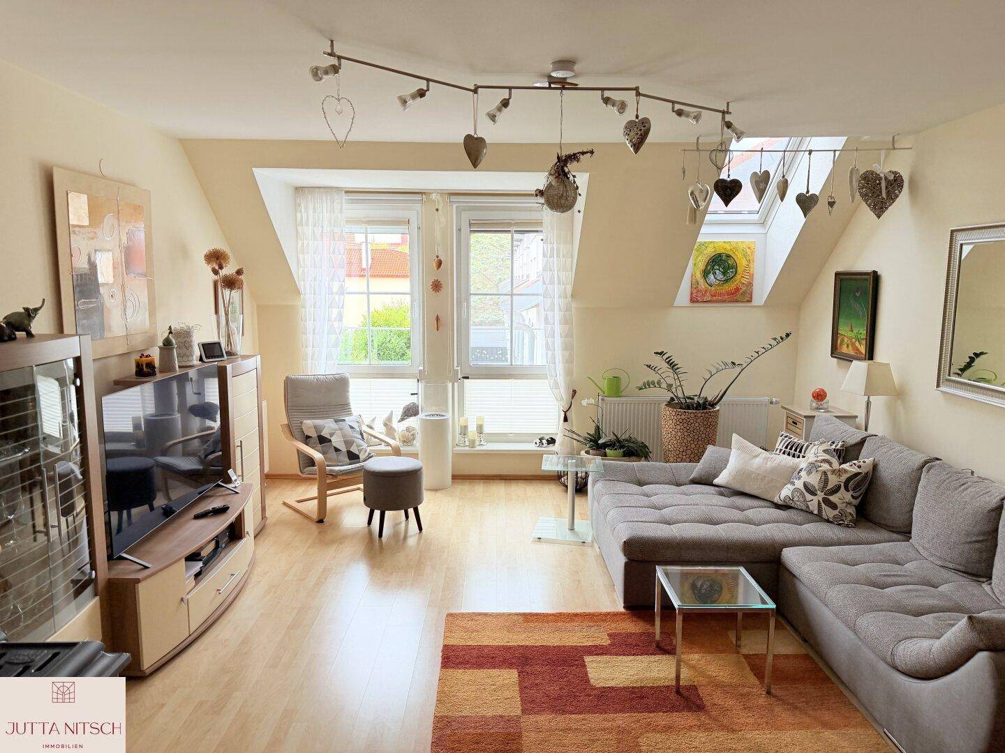 Helles Wohnzimmer mit Dachschrägen, Holzboden und gemütlicher Sitzecke am Fenster.