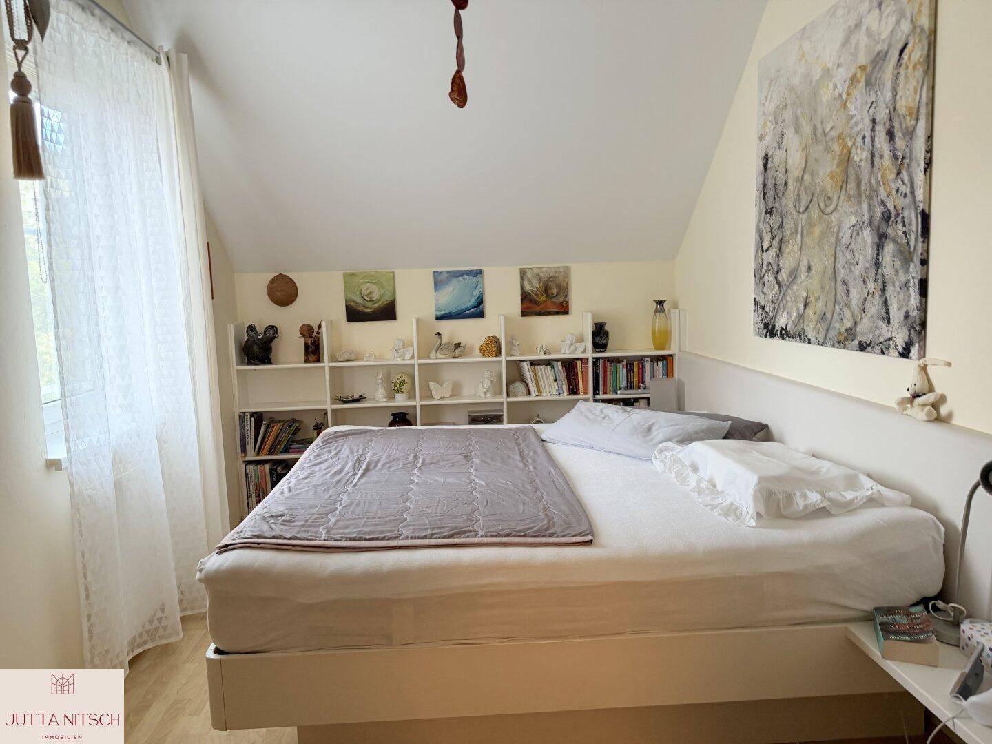 Schlafzimmer mit Dachschräge, Doppelbett und integrierten Bücherregalen an der Wand.