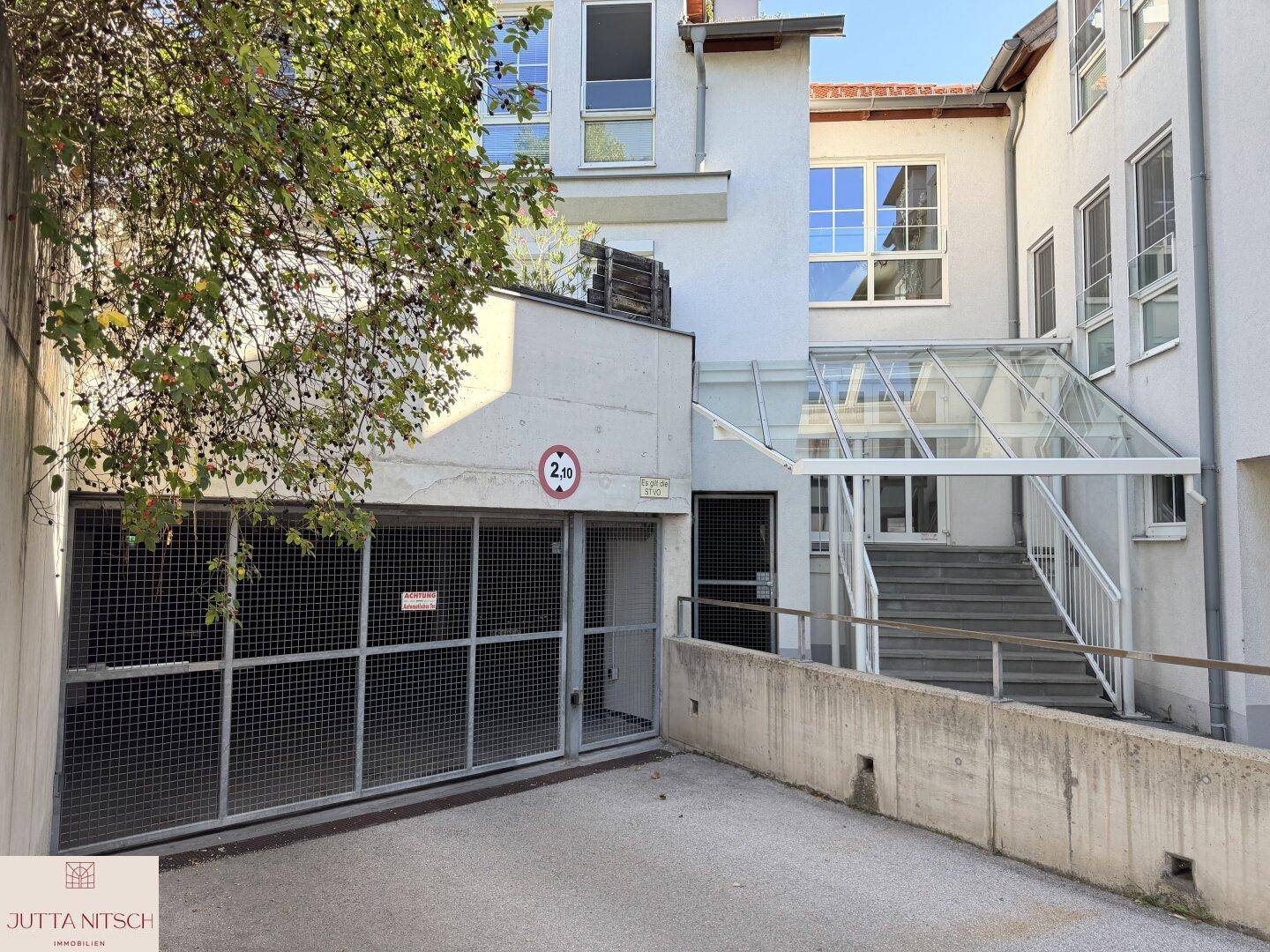 Eingangsbereich des Gebäudes mit Treppe und Zufahrt zur Tiefgarage unter blauem Himmel.