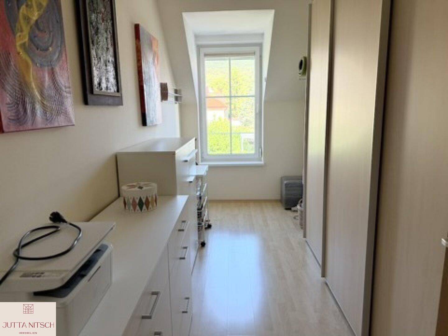 Schmaler Raum mit Dachschräge, Fenster und praktischen weißen Schränken.