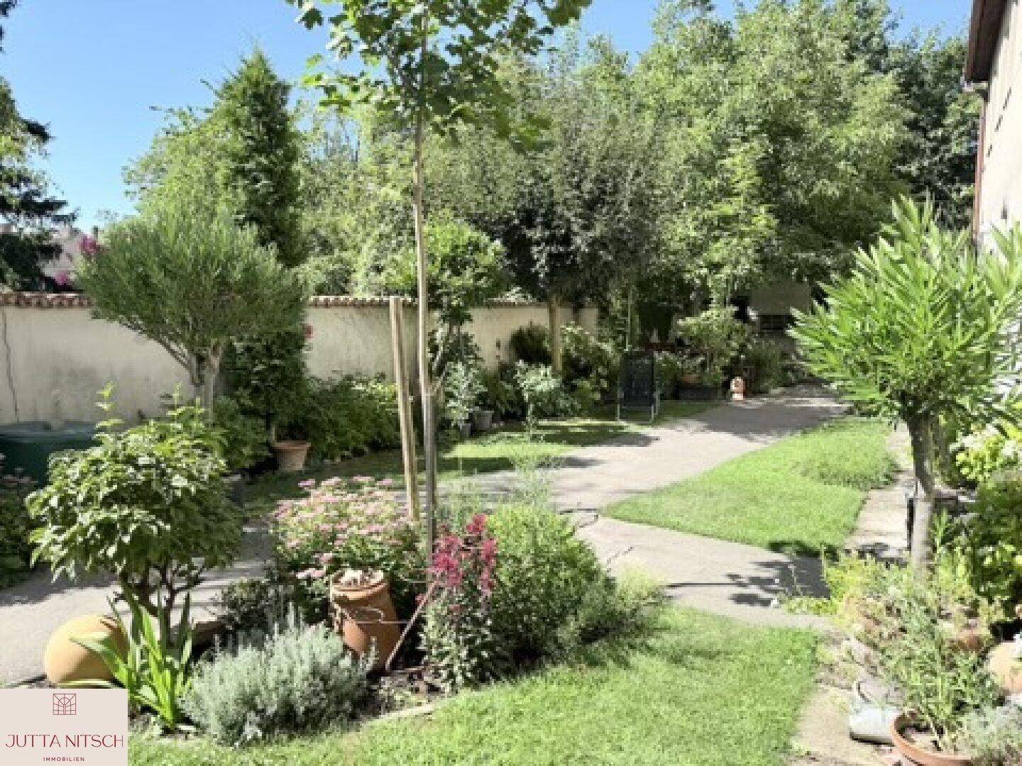 Großer, gepflegter Garten mit Rasenfläche, Bäumen, Sträuchern und einem Grillbereich im Hintergrund.