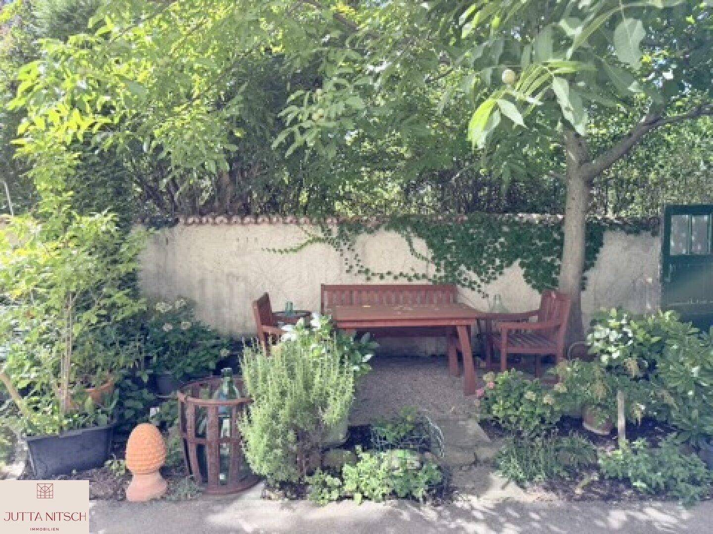 Gemütlicher Essbereich im Garten unter schattenspendenden Bäumen, mit Holztisch und Bänken.