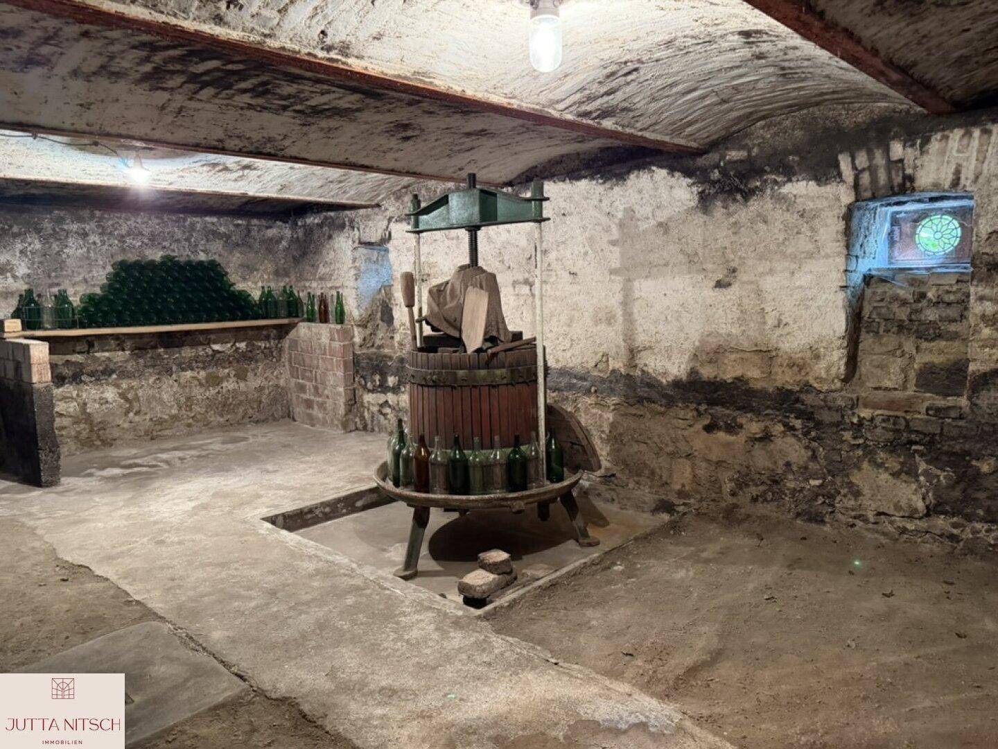 Historischer Kellerraum mit Steinmauern, einem alten Weinkeller und Flaschen, die eine rustikale Atmosphäre schaffen.