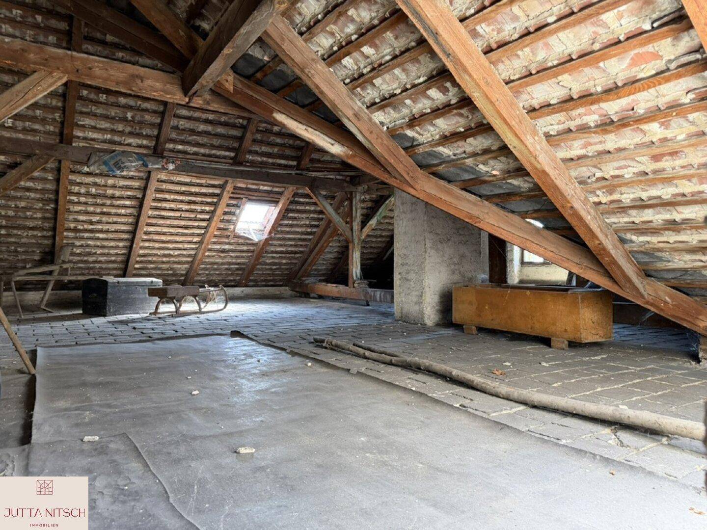 Geräumiger Dachboden mit sichtbaren Holzbalken und einem Dachfenster, das natürliches Licht hereinlässt.