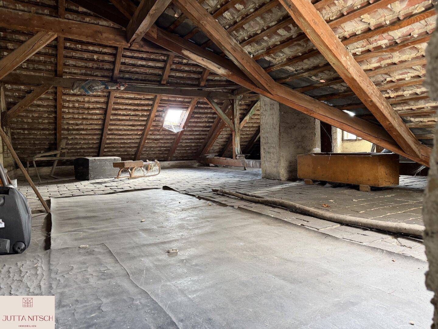 Unfertiger Dachboden mit sichtbaren Holzbalken, Dachfenster und viel Potenzial für einen Ausbau.