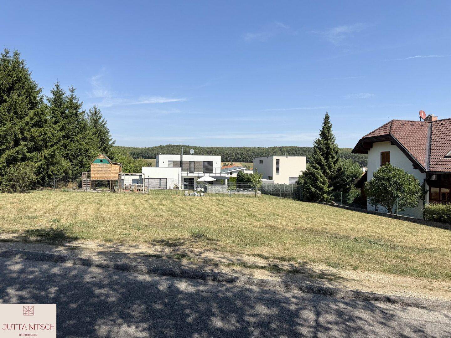 Weitläufiges Grundstück mit Blick auf moderne Häuser und grüne Umgebung unter blauem Himmel.