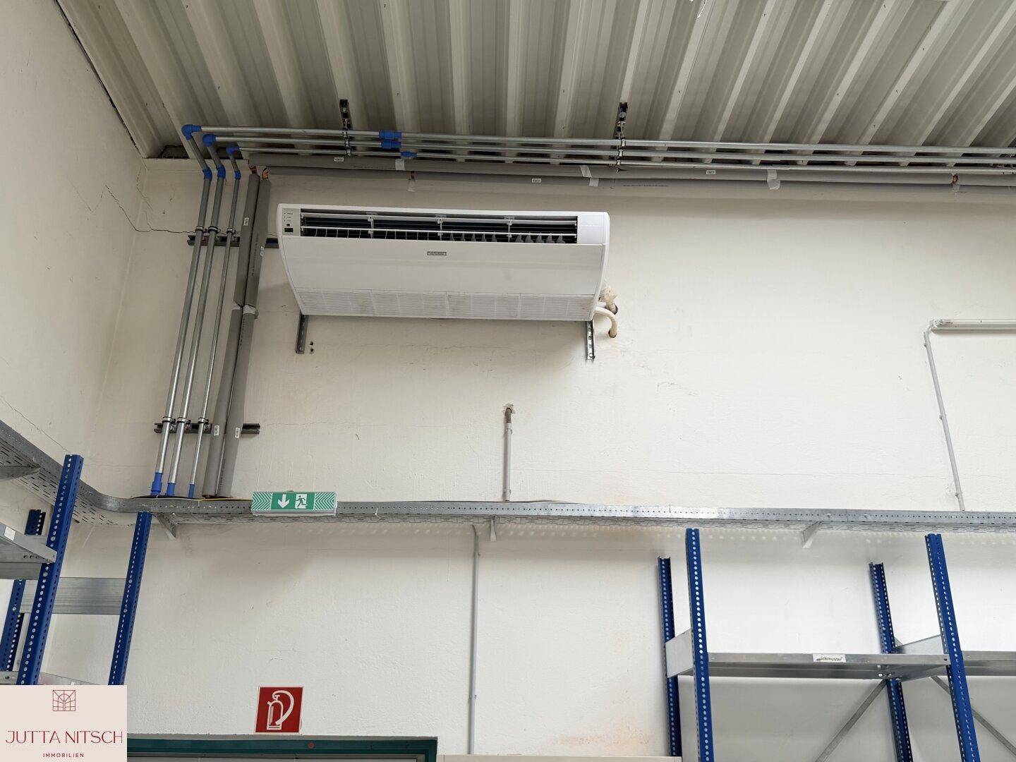 Wandbereich in einem Lagerraum mit installierter Klimaanlage und sichtbaren Leitungen und Regalen.