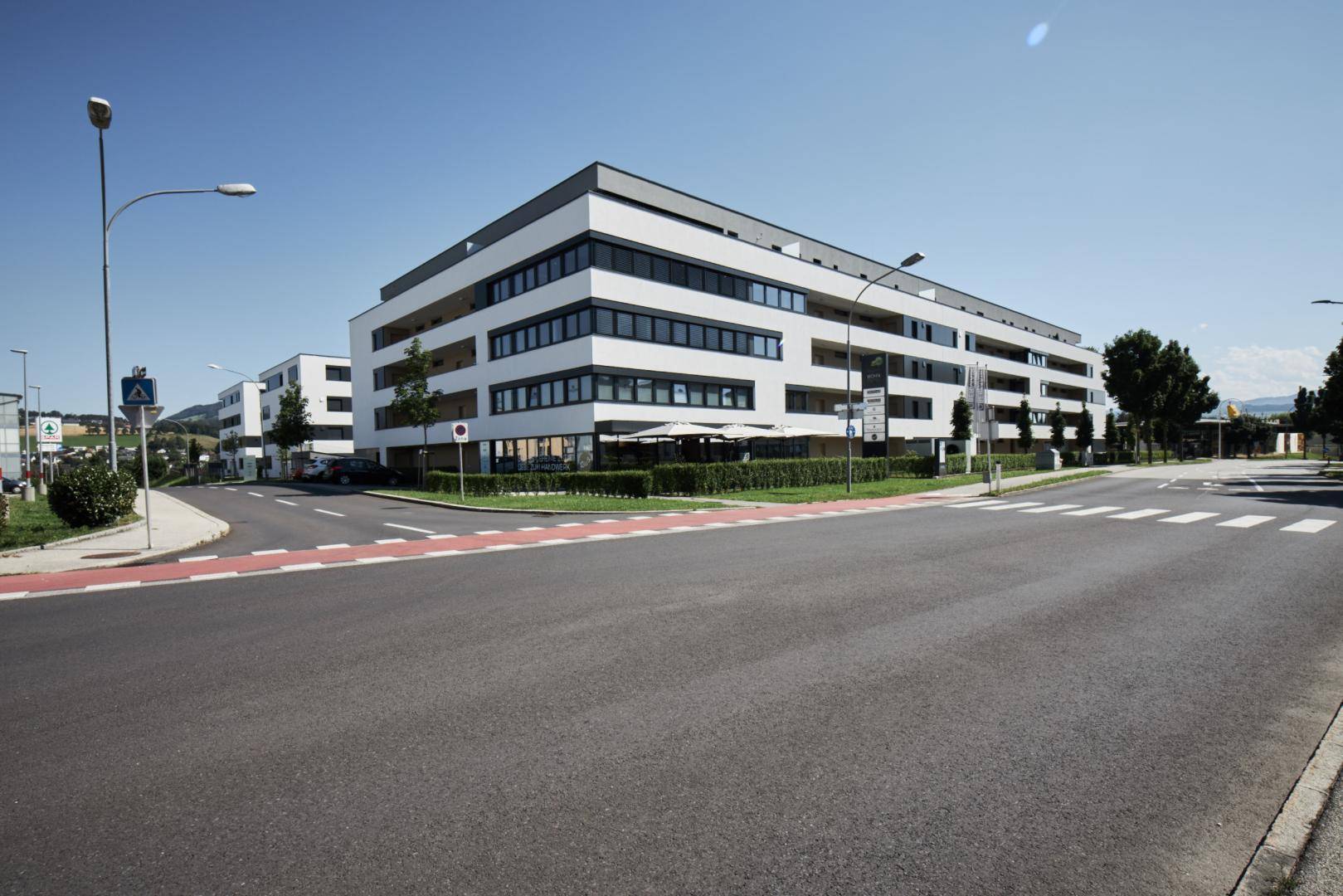 Modernes Wohngebäude mit klaren Linien, großen Fenstern und Balkonen an einer Straße.