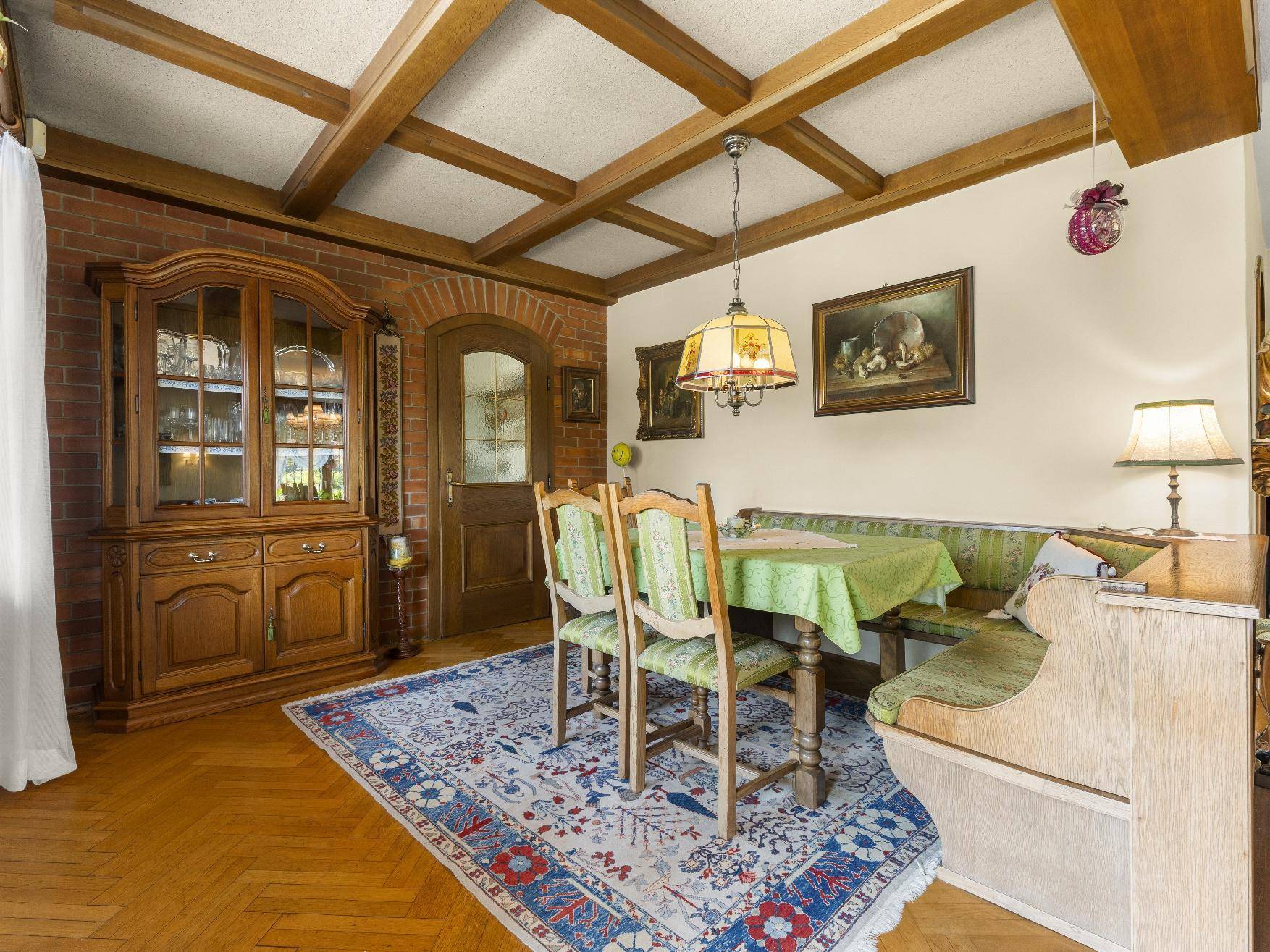 Gemütliches Esszimmer mit Holzbalkendecke, traditionellen Möbeln und Teppichboden.