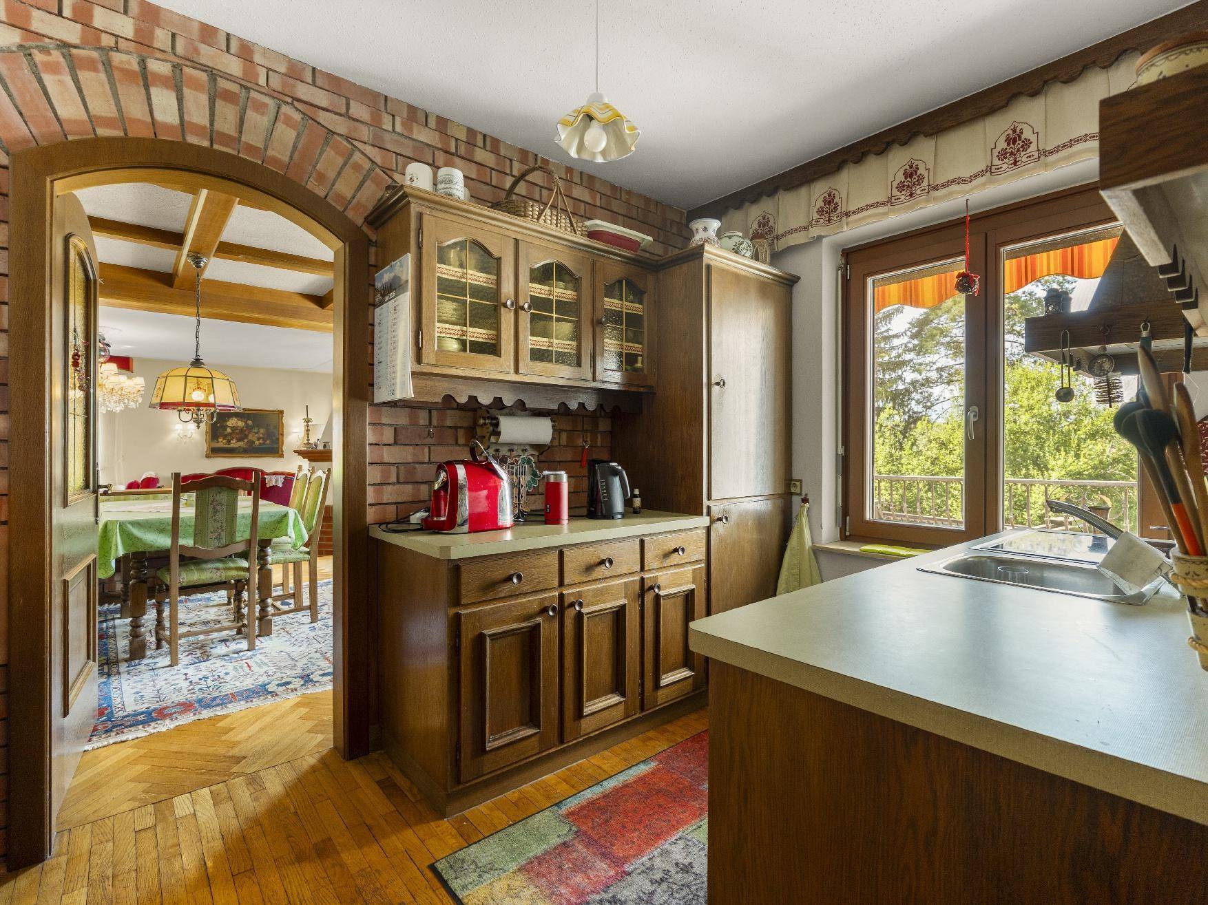 Traditionelle Küche mit Holzschränken, Backsteinwand und Blick ins Esszimmer.