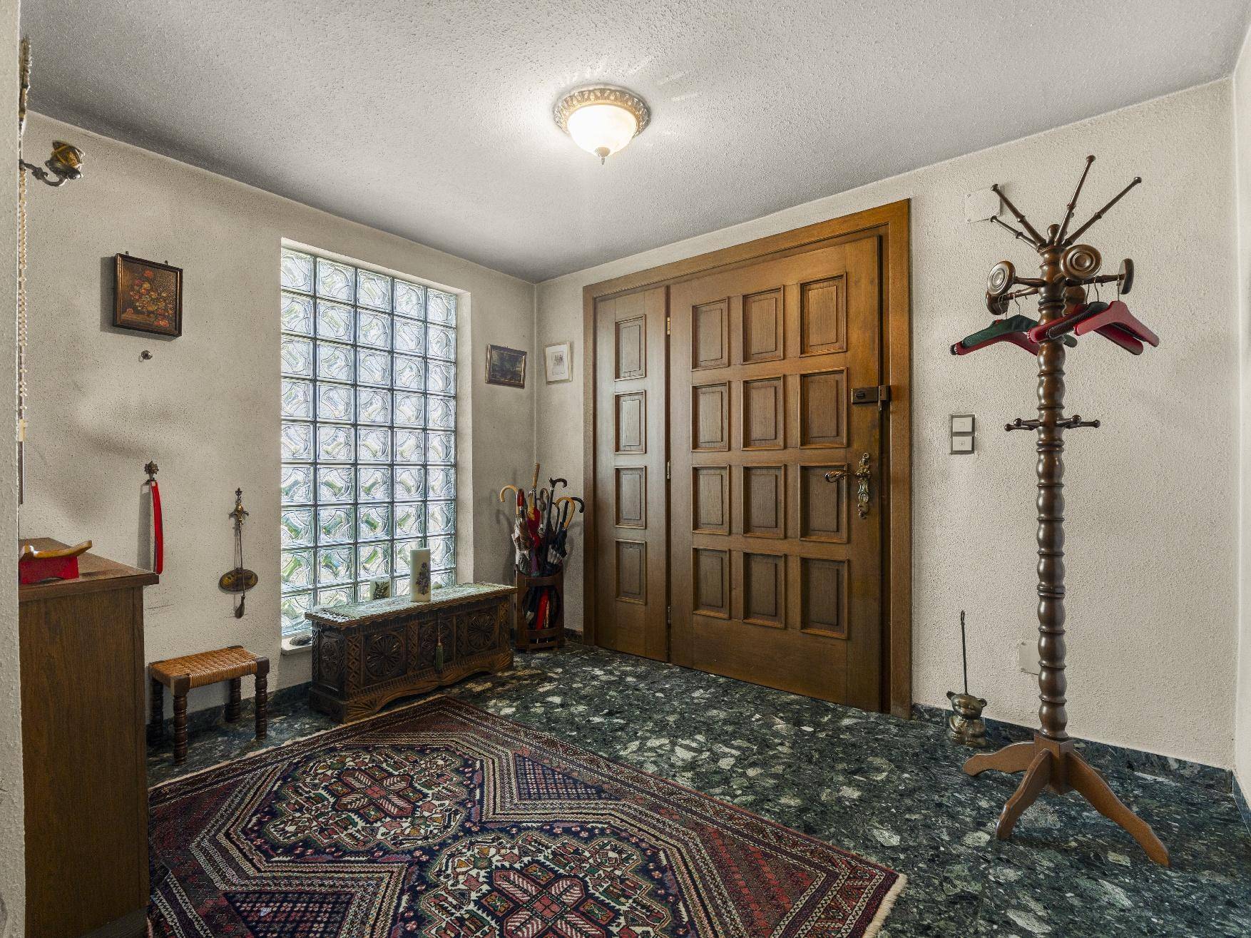 Geräumiger Eingangsbereich mit dunklem Terrazzoboden, Holzdoppeltür und Garderobe.