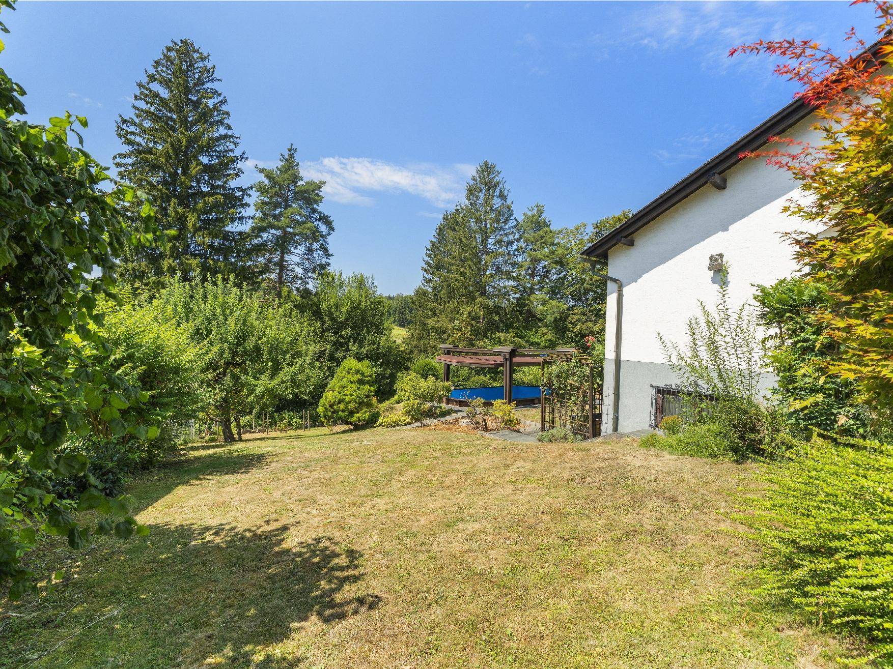 Seitlicher Blick auf das Haus mit weitläufigem Rasen und dem Poolbereich im Hintergrund.