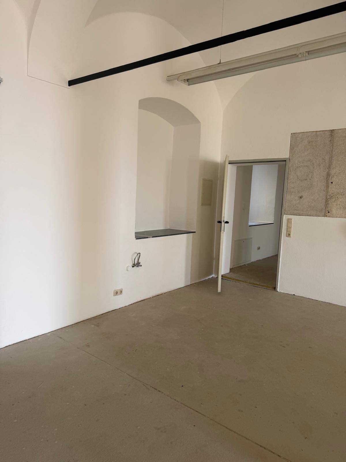 Geräumiger, heller Raum mit Gewölbedecke, einer Tür und einer Nische in der Wand.