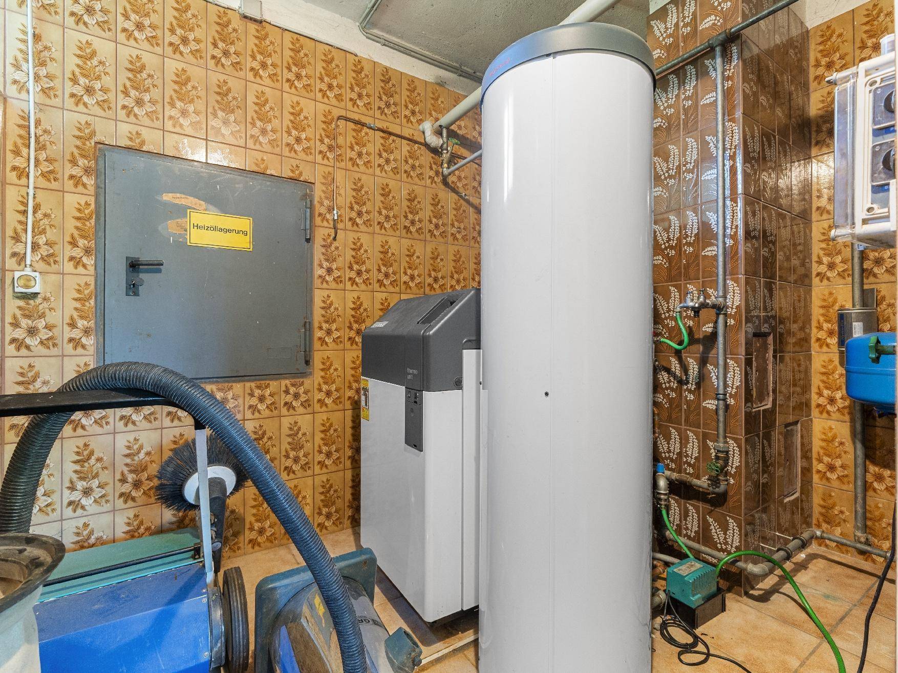 Heizungsraum mit Warmwasserspeicher und technischen Installationen in gefliestem Bereich.